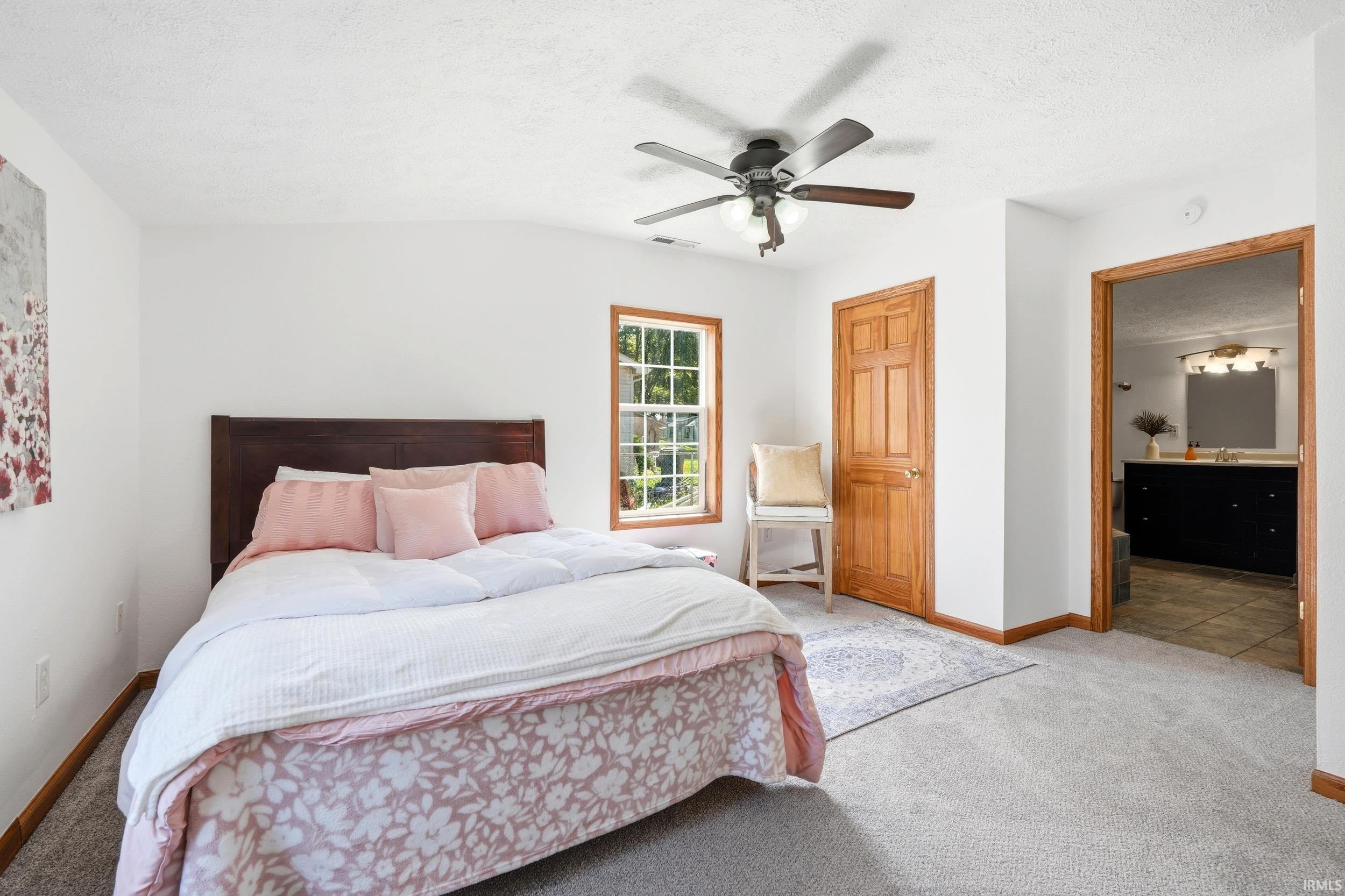 Carpeted bedroom featuring a ceiling fan with integrated lighting, a window with natural wood trim, and a natural wood door