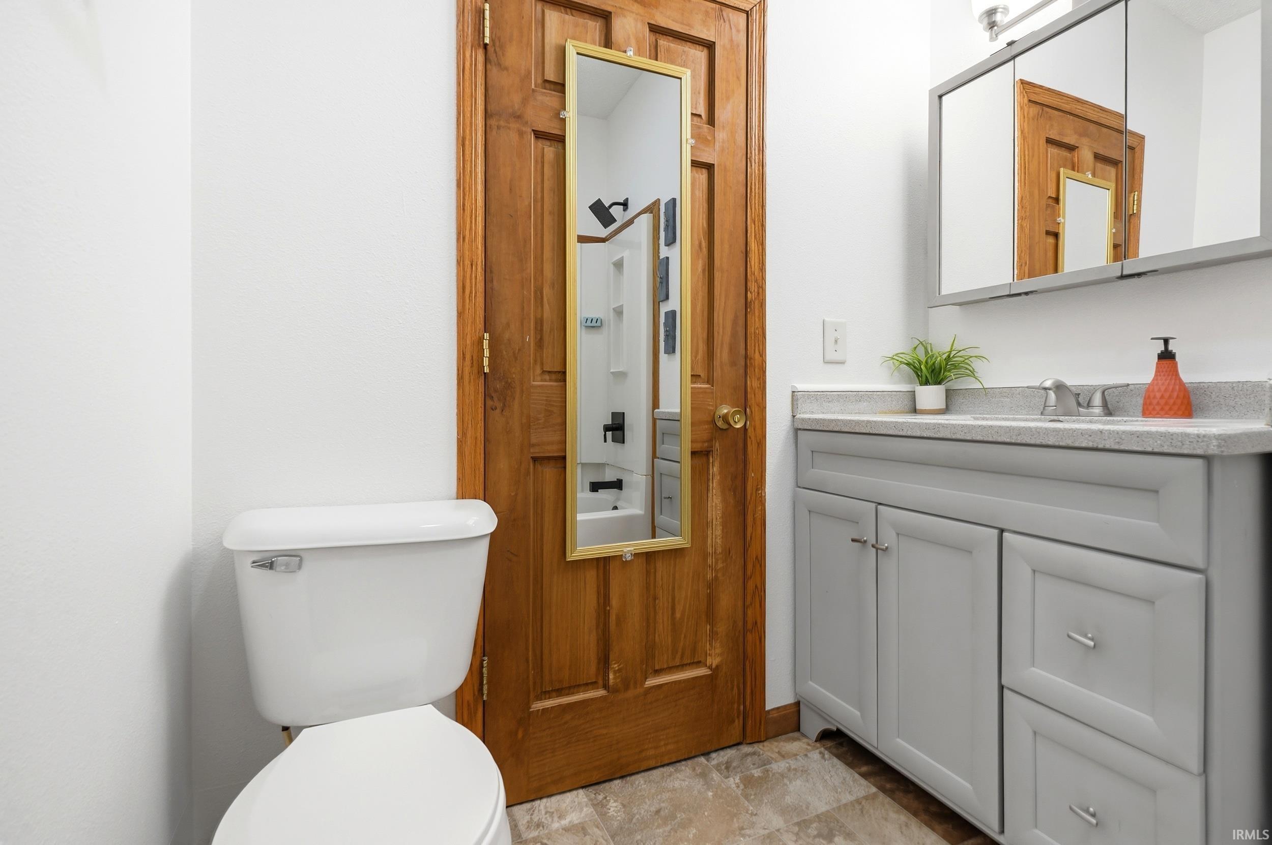 Bathroom vanity with light gray shaker-style cabinetry, a light-toned countertop, and a recessed medicine cabinet featuring mirrored doors