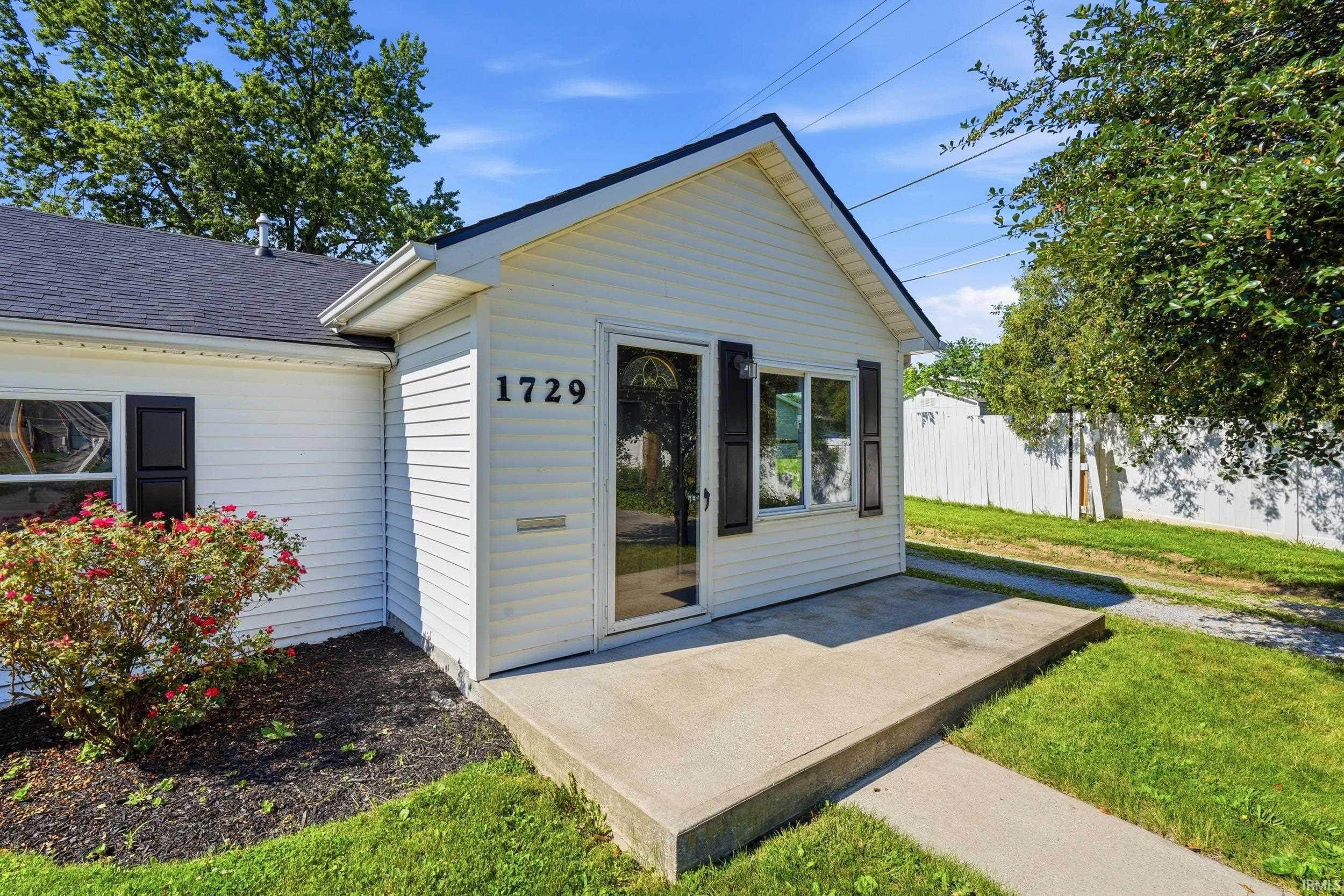 White siding exterior with a dark shingled roof, featuring a concrete front stoop, full-light entry door, and dark louvered shutters