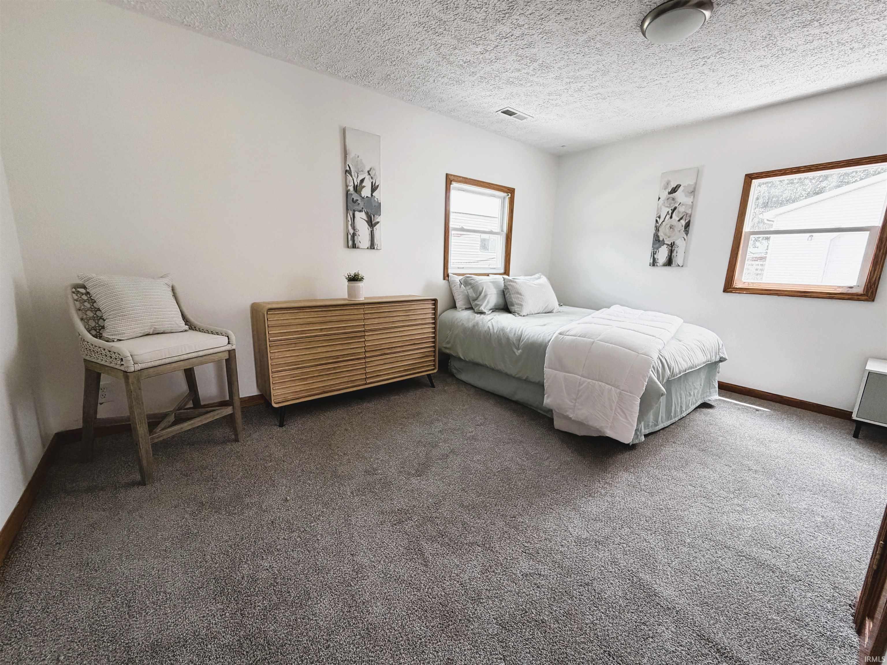 Bedroom featuring two windows with wood trim, gray carpeting, and a white ceiling with a flush-mount light fixture