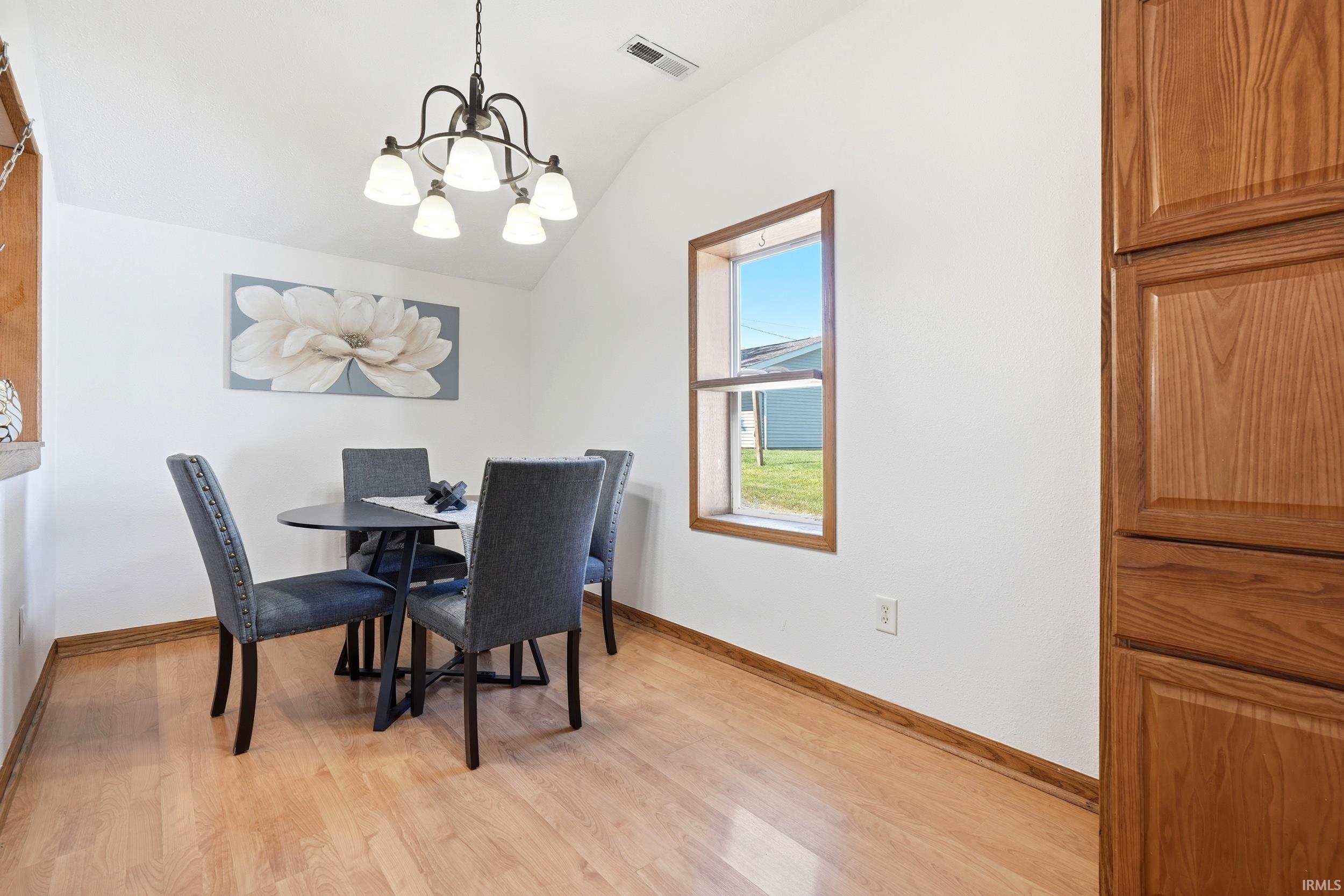 Vaulted ceiling dining area featuring wood-finish flooring, a contemporary chandelier, and a window with wood trim