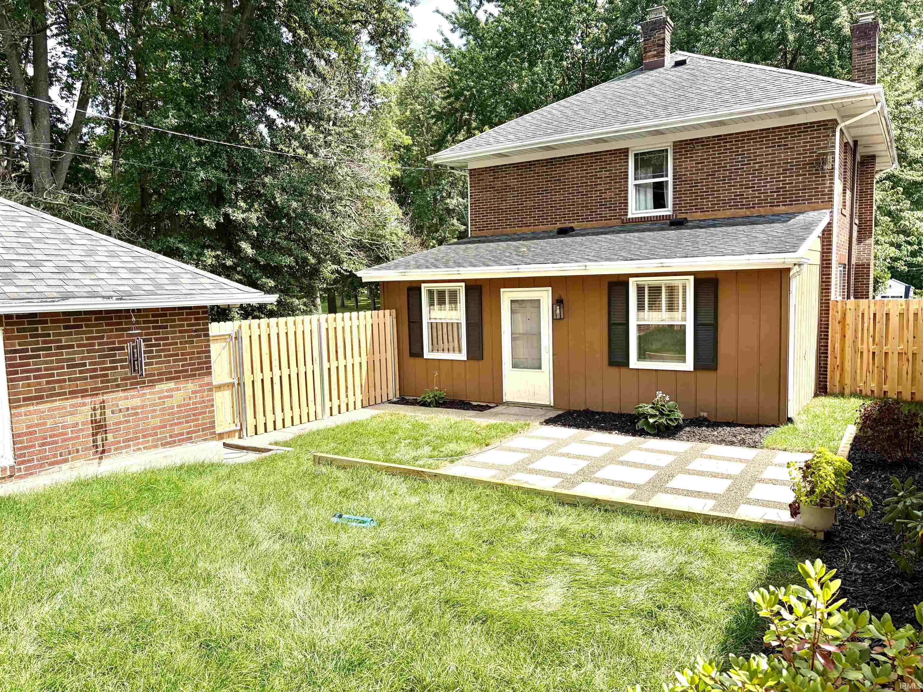 Rear exterior featuring a brown siding addition, white entry door with an overhead light fixture, and a window with dark shutters