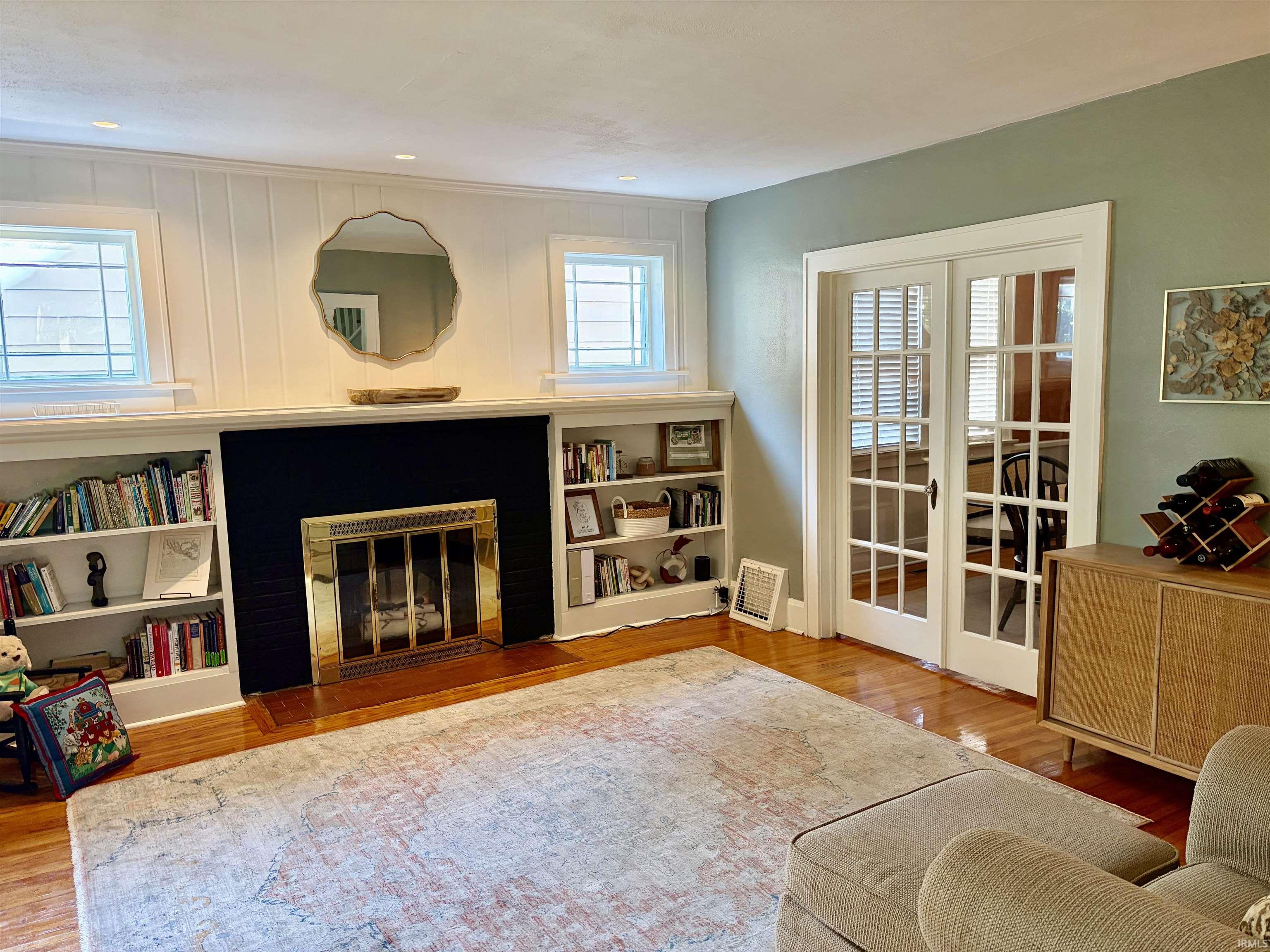 Living area featuring a fireplace with a black surround and brass-toned screen, built-in shelving, polished wood-finish flooring, and French doors