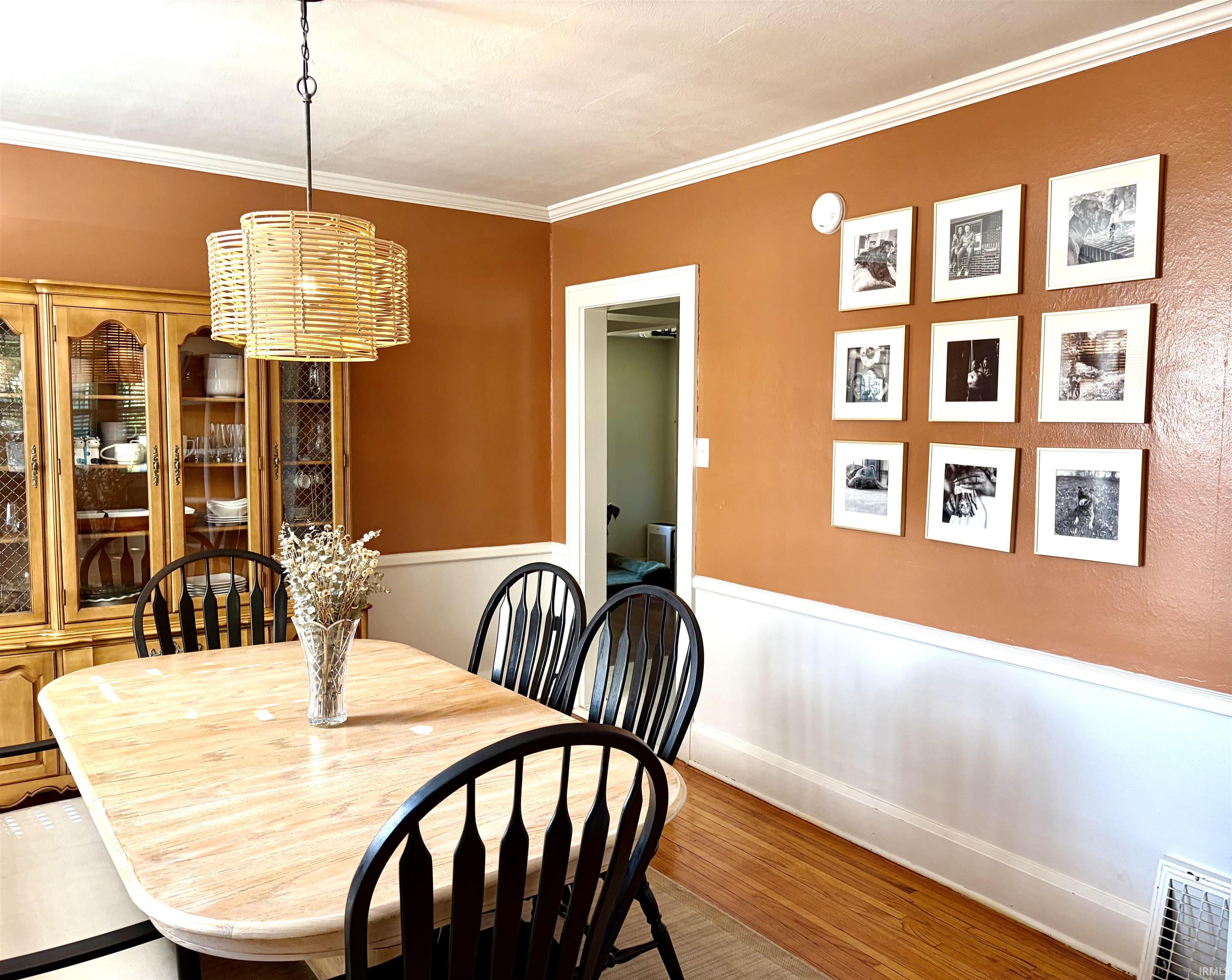 Dining area featuring hardwood flooring, white crown molding, and a woven pendant light fixture