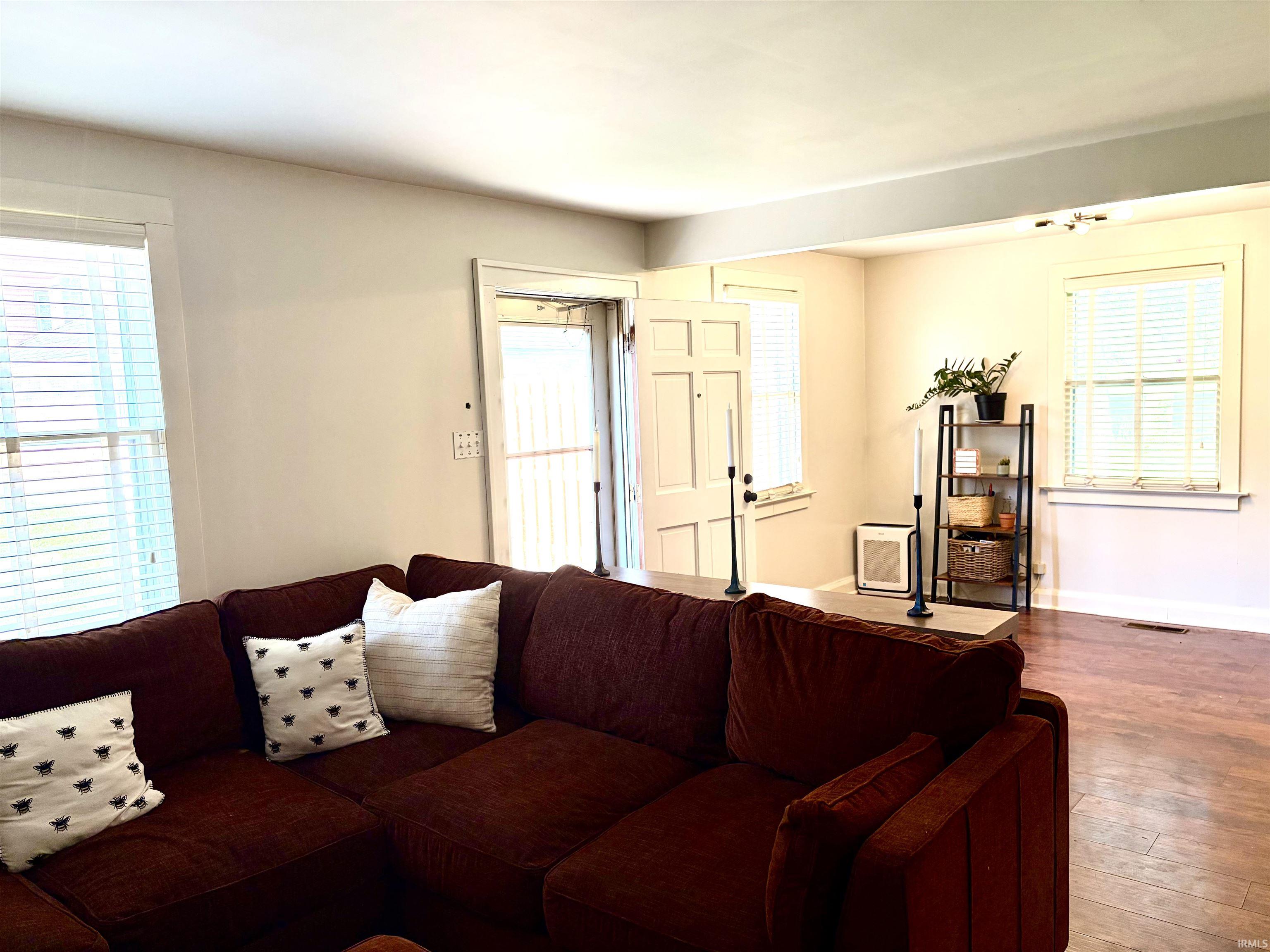 Living area featuring wood-finish flooring, light-toned wall paint, and multiple windows with blinds