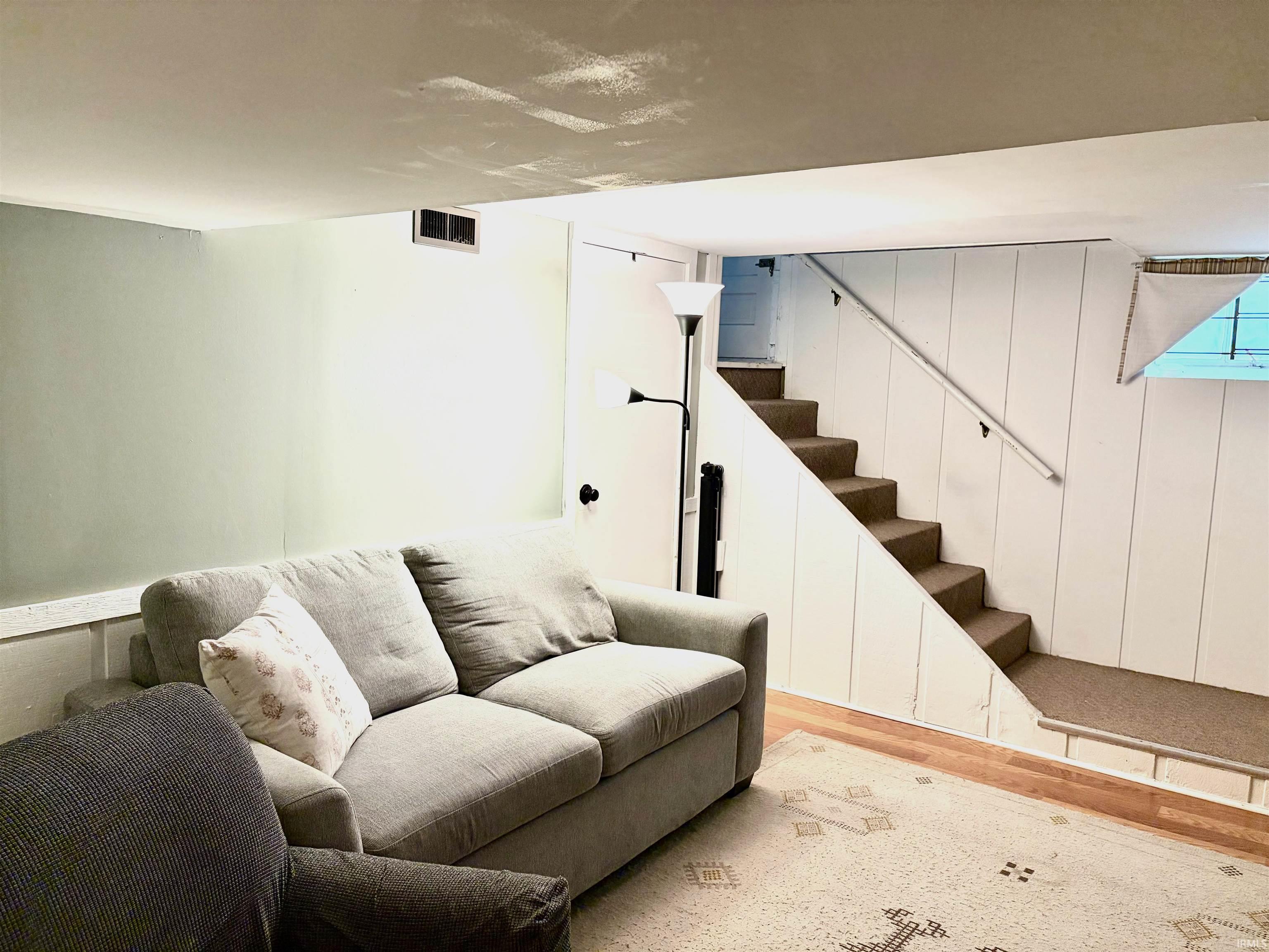 Finished lower level featuring wood-finish flooring, a carpeted staircase with a handrail, and white paneled walls