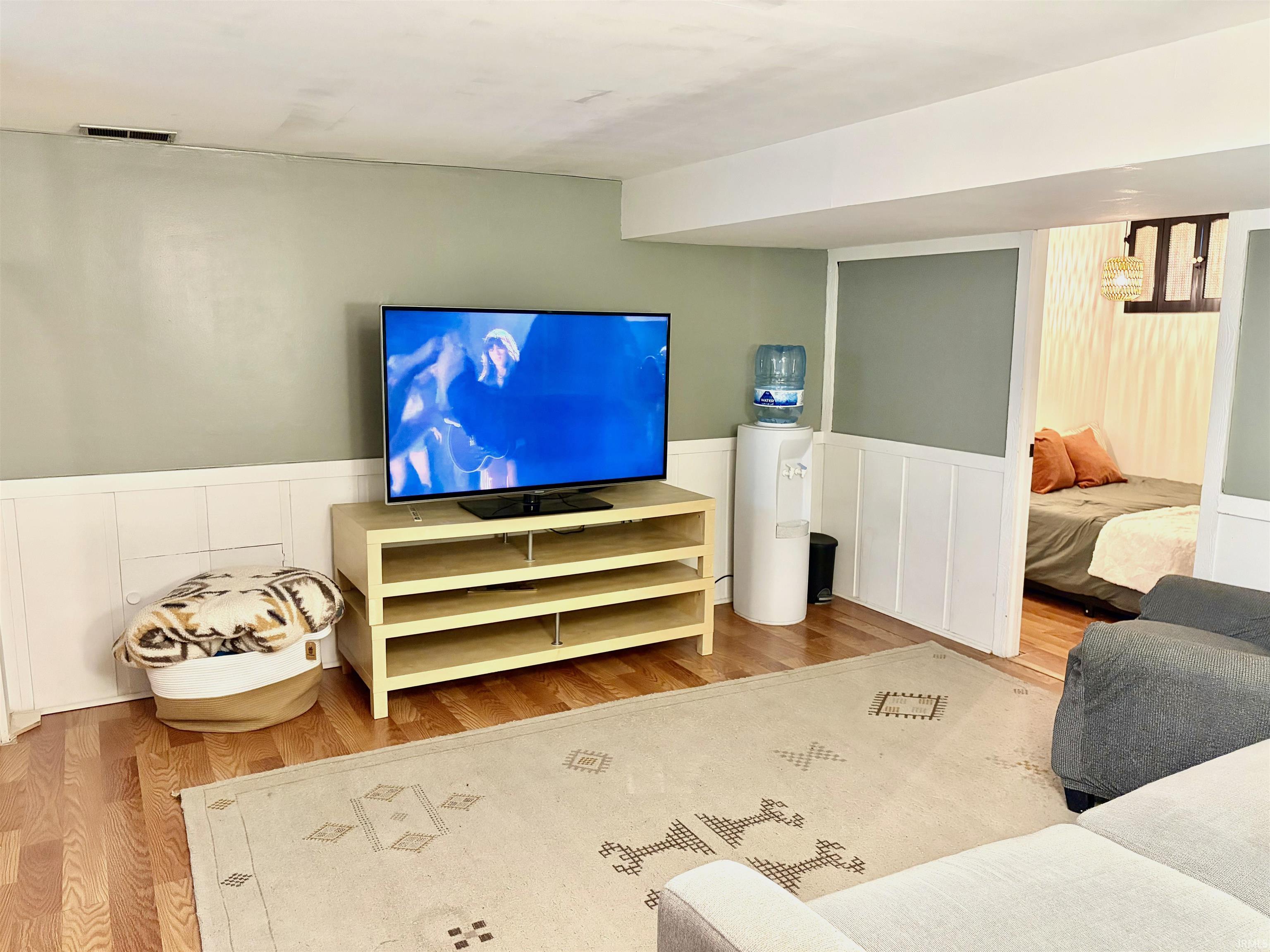 Entertainment space featuring hardwood-finish flooring, a neutral area rug, and wainscoting