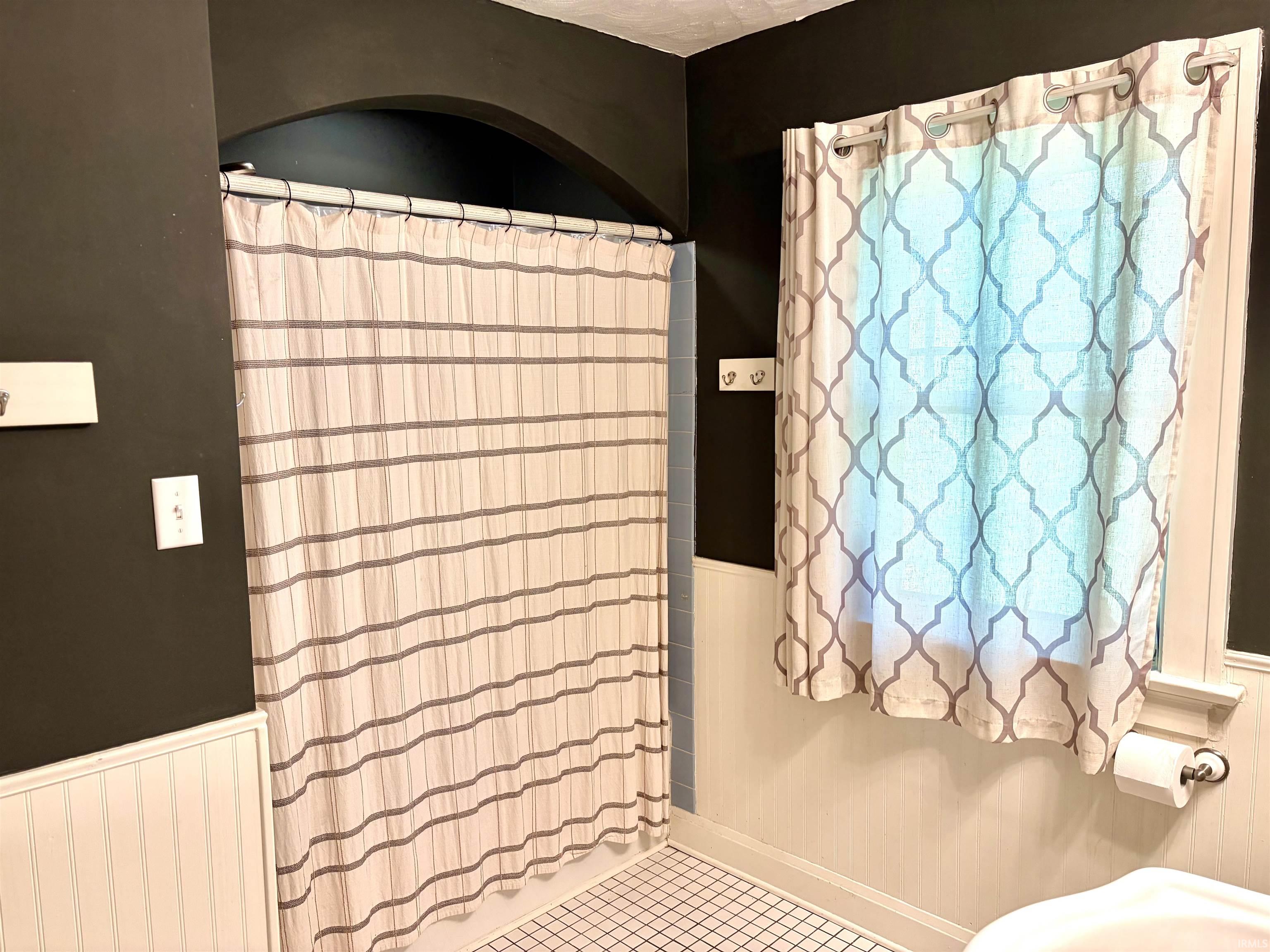 Bathroom featuring wainscoting, an arched shower enclosure, and grid-pattern floor tiling