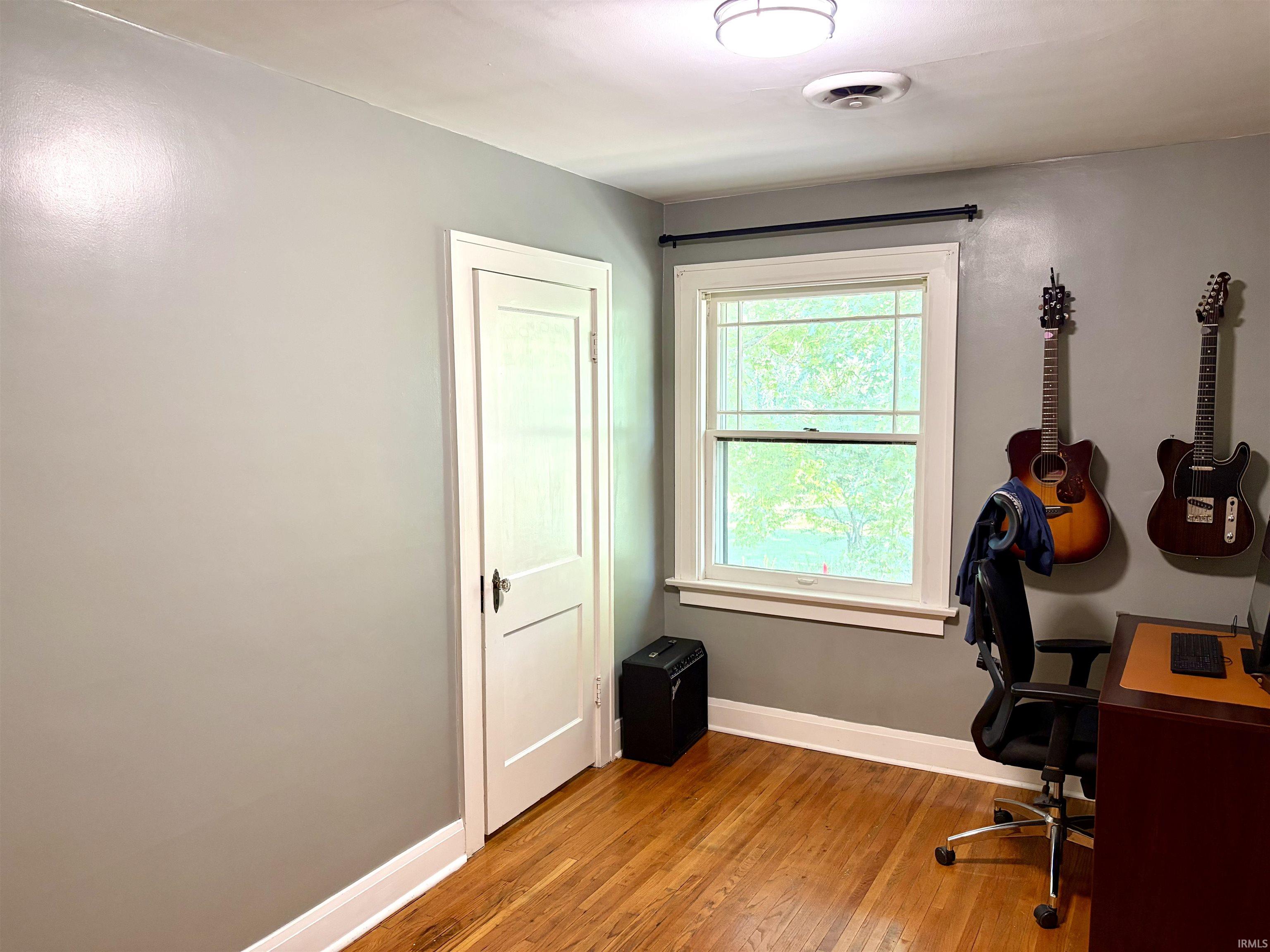Hardwood flooring with a single window featuring white trim and a black curtain rod