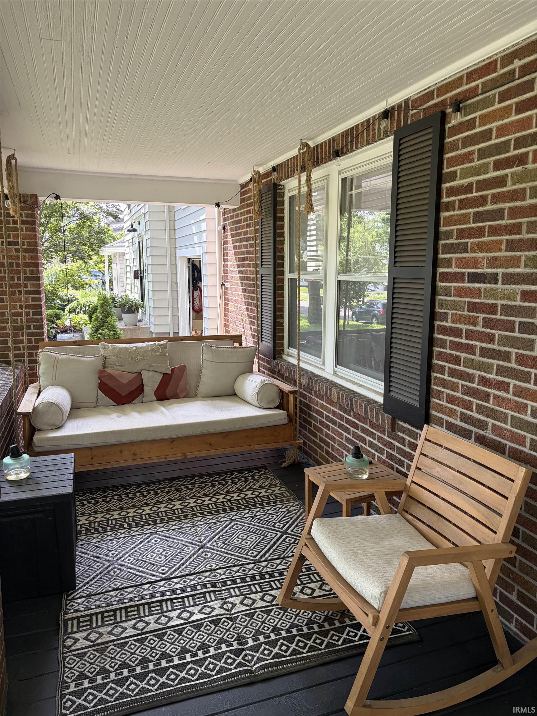 Brick exterior featuring a covered porch with a beadboard ceiling, painted floor, and multi-pane windows with louvered shutters