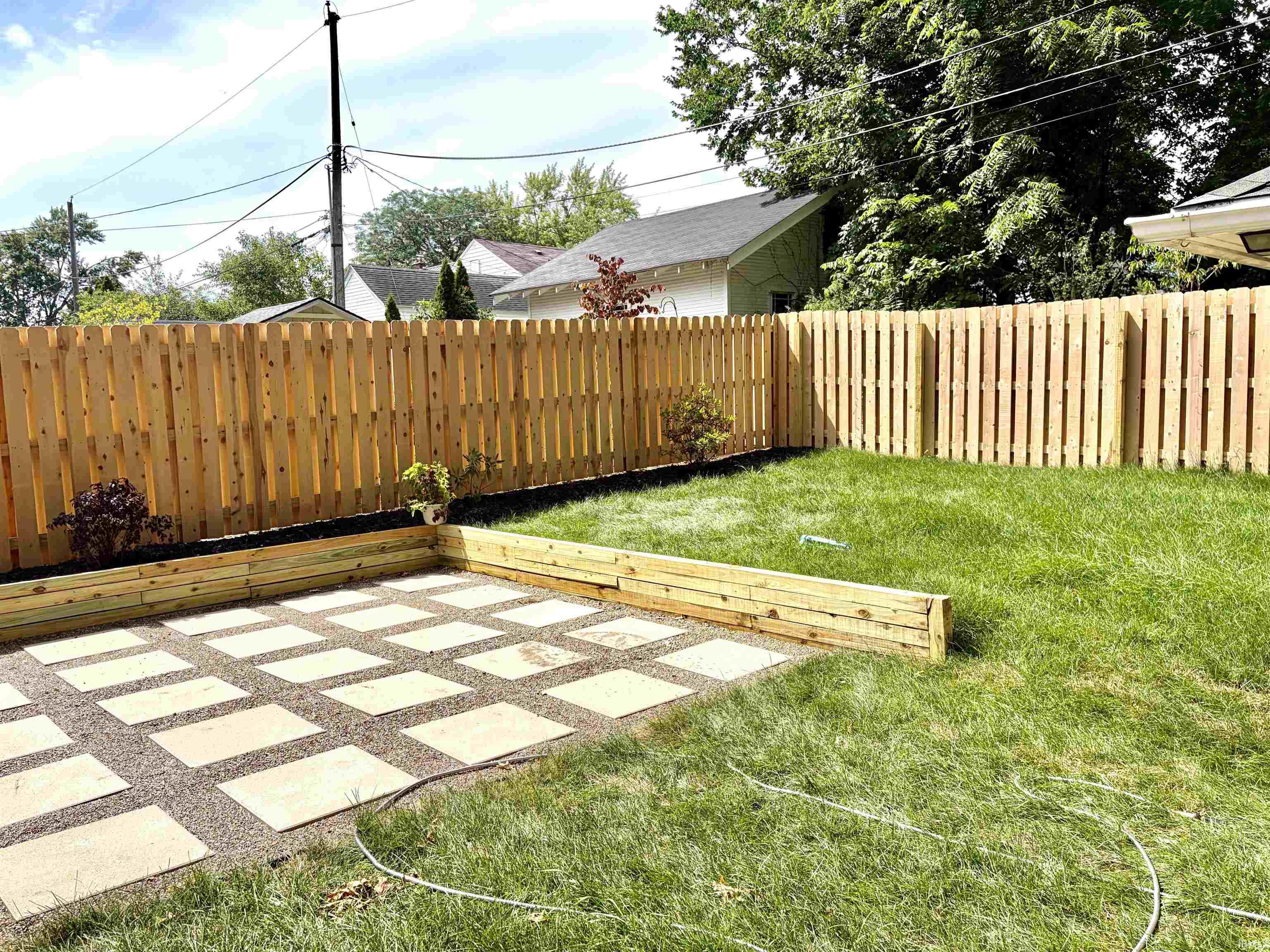 Expansive backyard featuring a new wood privacy fence, a rectangular patio with square pavers, a manicured lawn, and raised garden beds