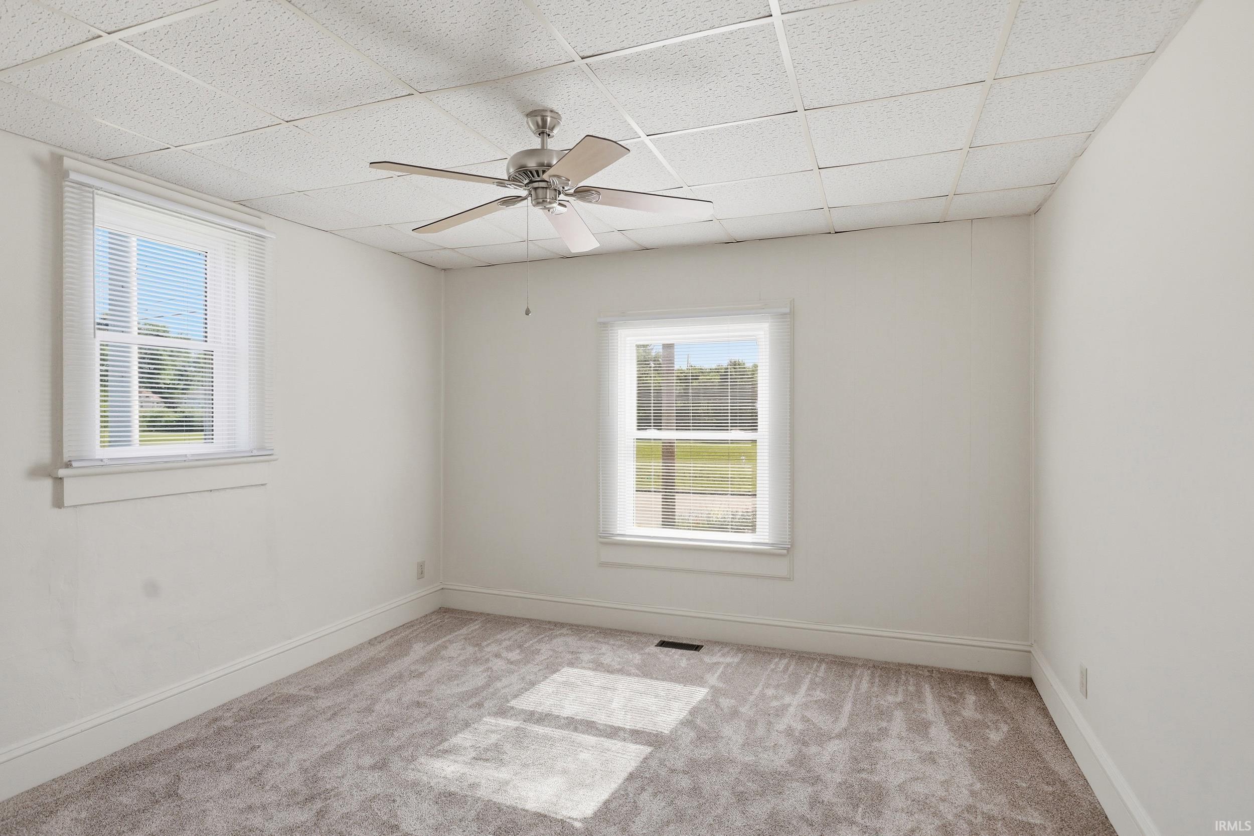 Carpeted room featuring a ceiling fan, two windows with blinds, white walls, and baseboard trim
