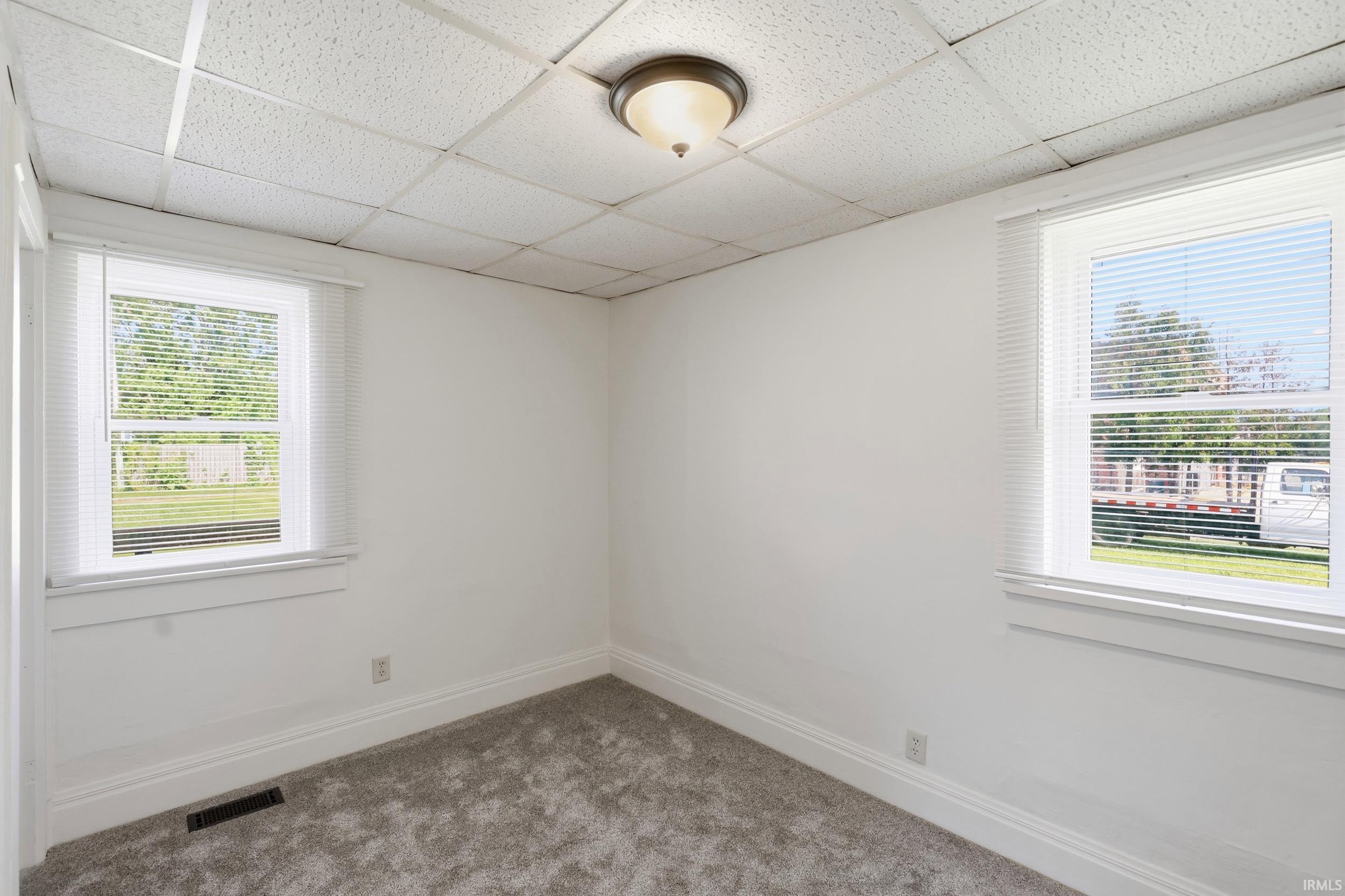 Bright room with two windows, showcasing white interior walls, white window blinds, and a neutral carpeted floor