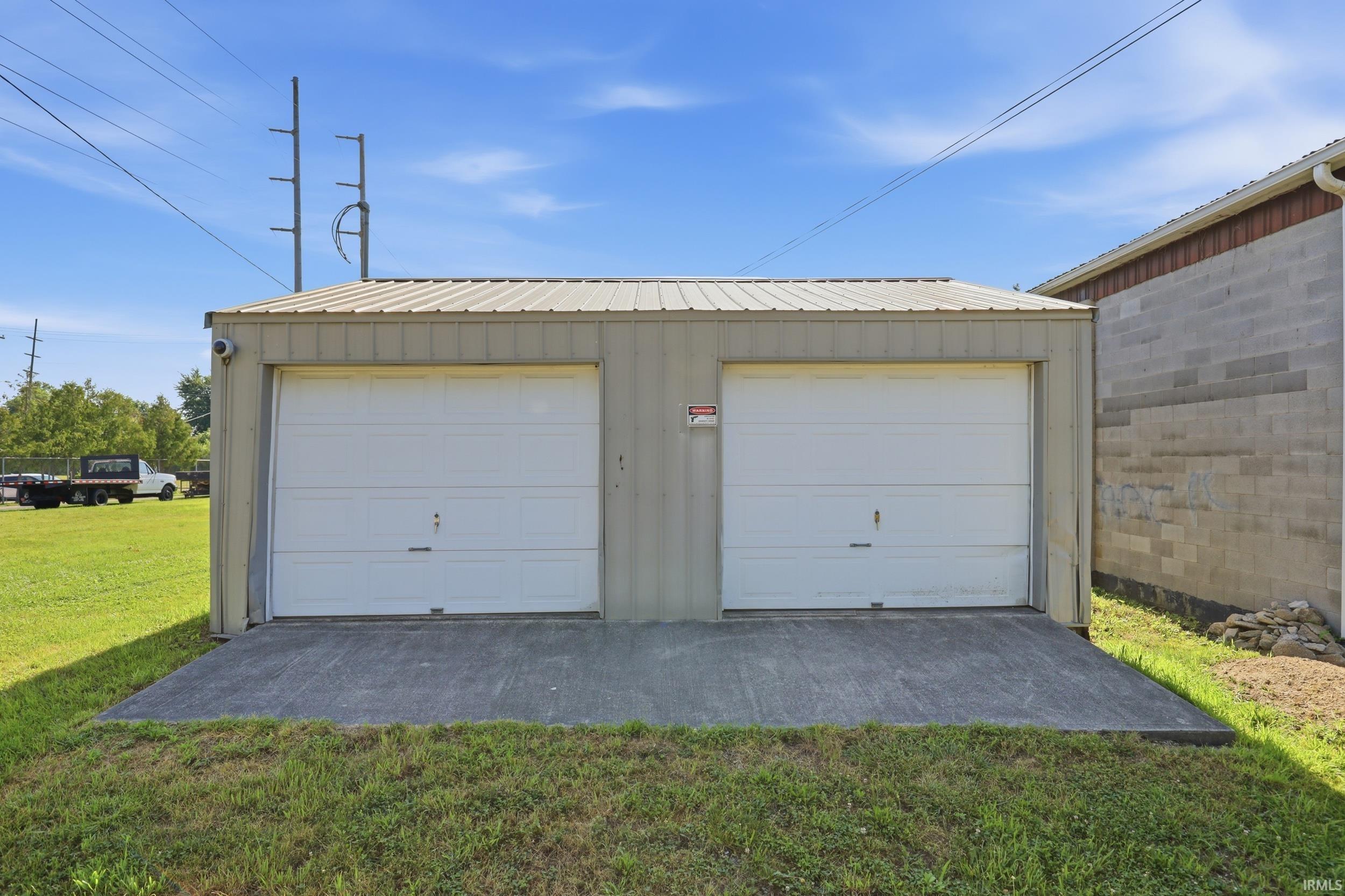 Two-bay metal garage structure featuring a metal roof, two white garage doors, and a concrete approach pad