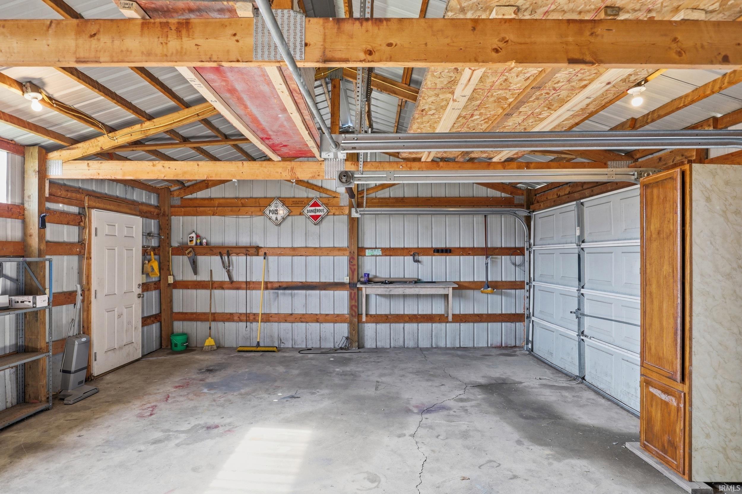 Spacious utility building featuring a concrete floor, exposed wood beam construction, corrugated metal wall panels, and two overhead garage doors