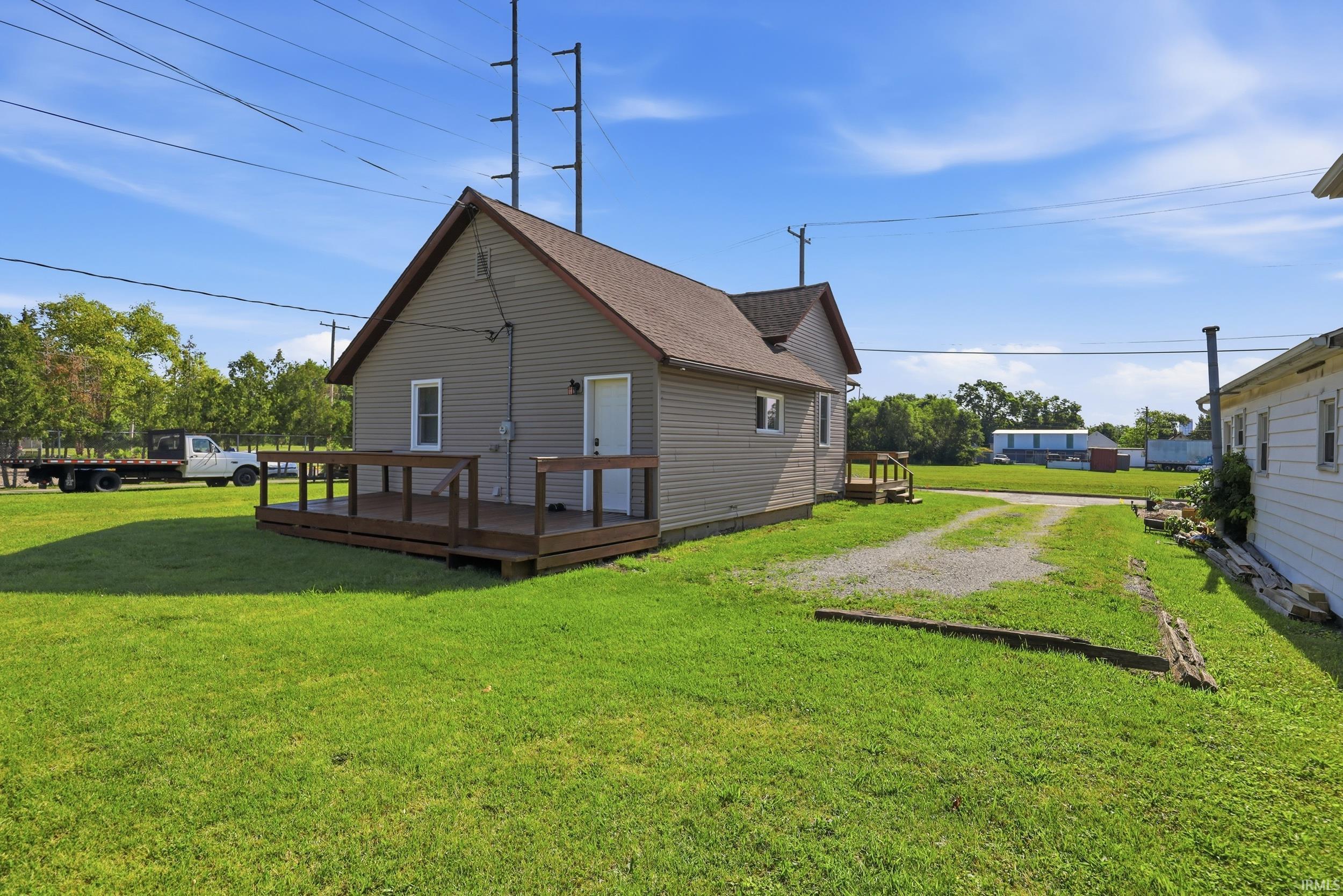 Exterior featuring light gray siding, a brown shingle roof, a full wooden deck, and a gravel driveway