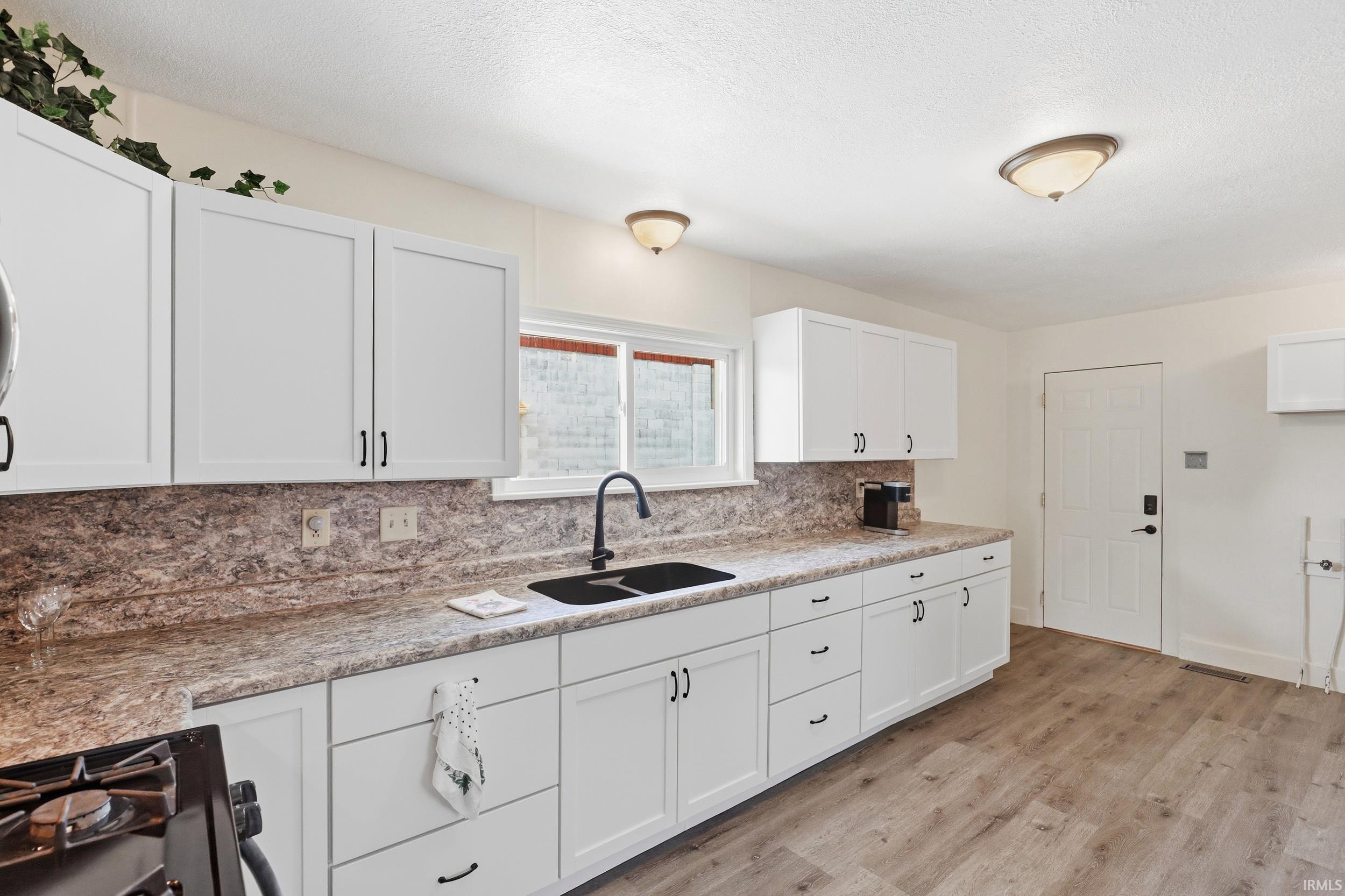 Kitchen featuring white cabinetry with dark hardware, a dark composite sink with a matte black faucet, and patterned countertops