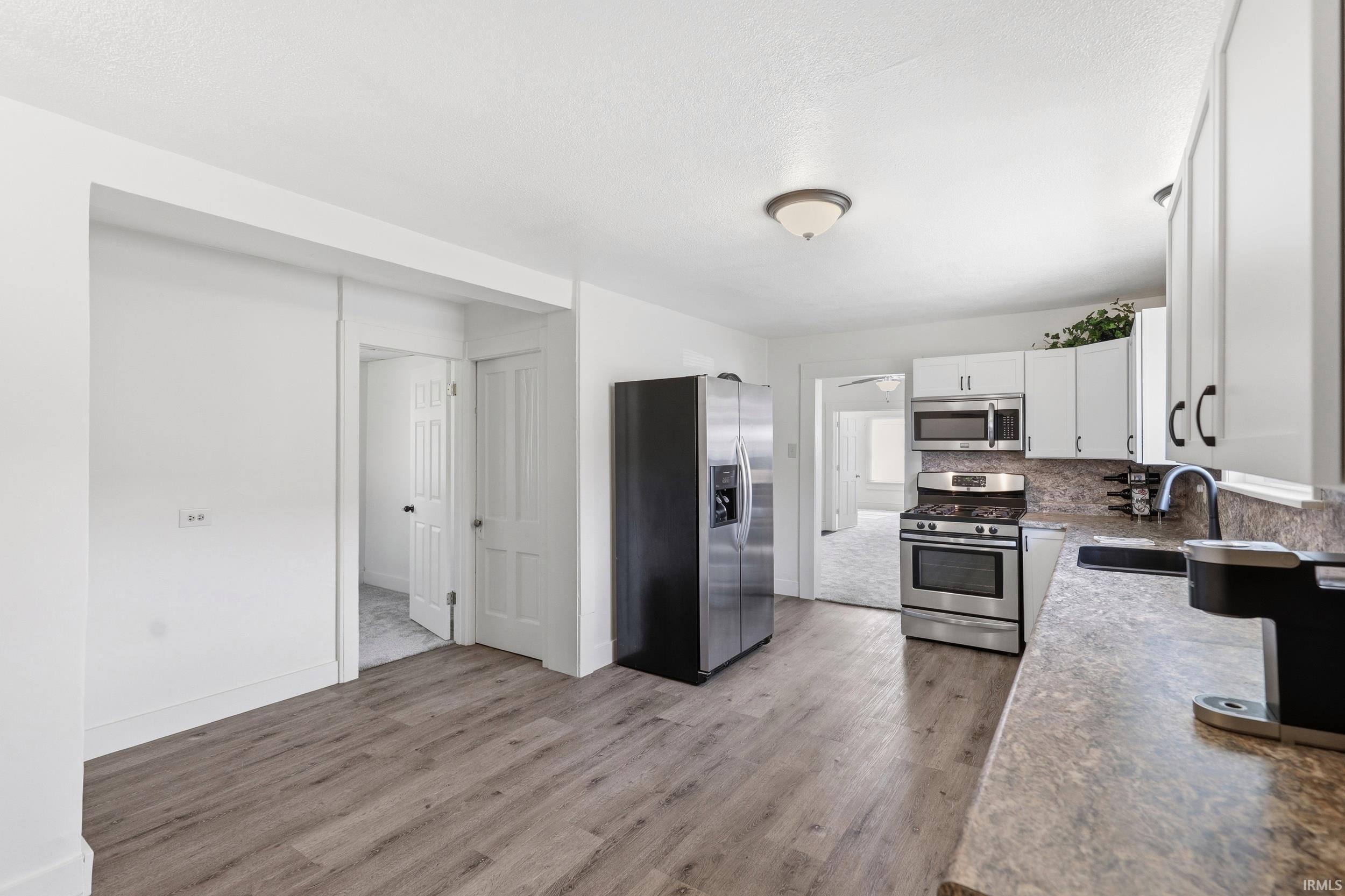Kitchen featuring wood-finish flooring, white cabinetry, stainless steel appliances, and a solid surface countertop