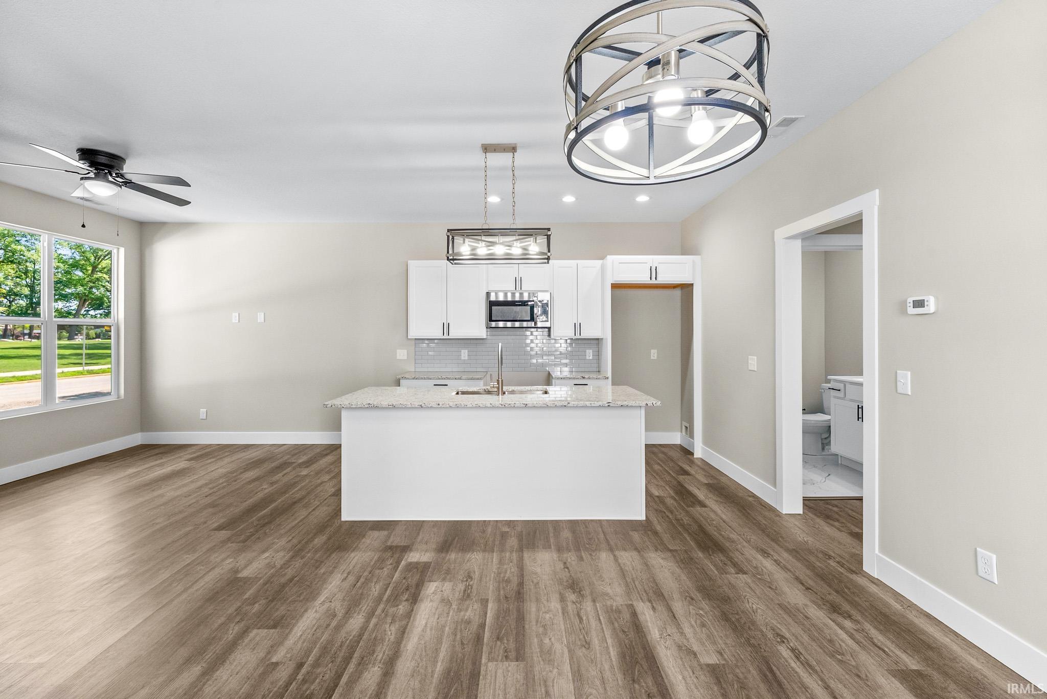 Open-concept living space featuring wood-finish flooring, a contemporary ceiling fan, and a kitchen island with stone countertops