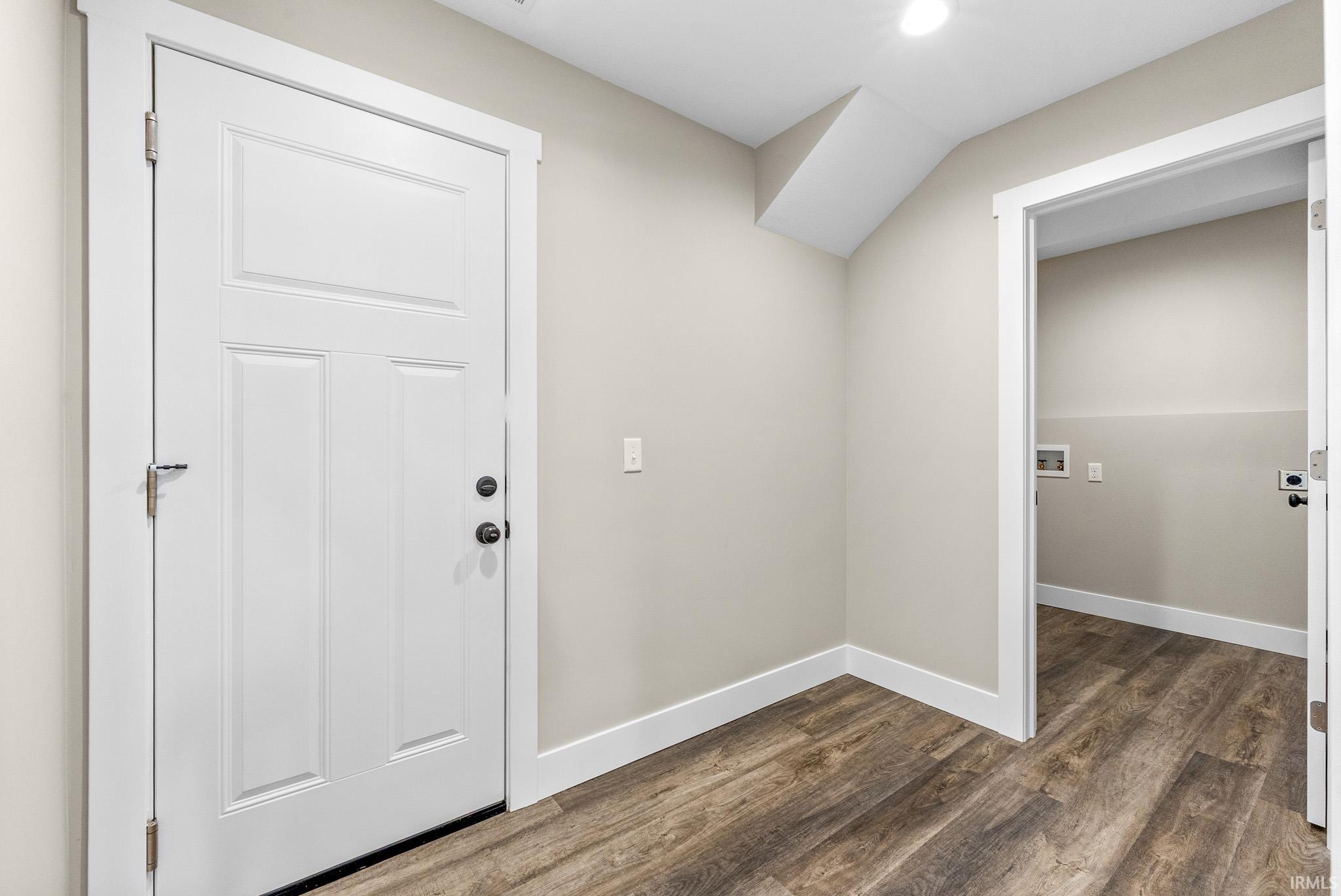 Mudroom featuring wood-finish flooring, white trim, and a paneled door with matte black hardware