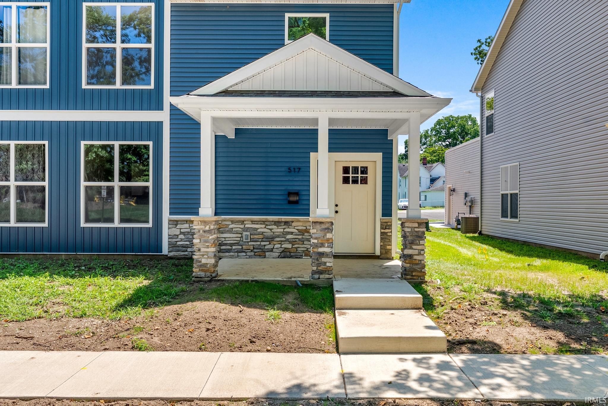Blue siding exterior with white trim, featuring a covered front porch with stone-wrapped columns and a light-colored entry door with grid window panes