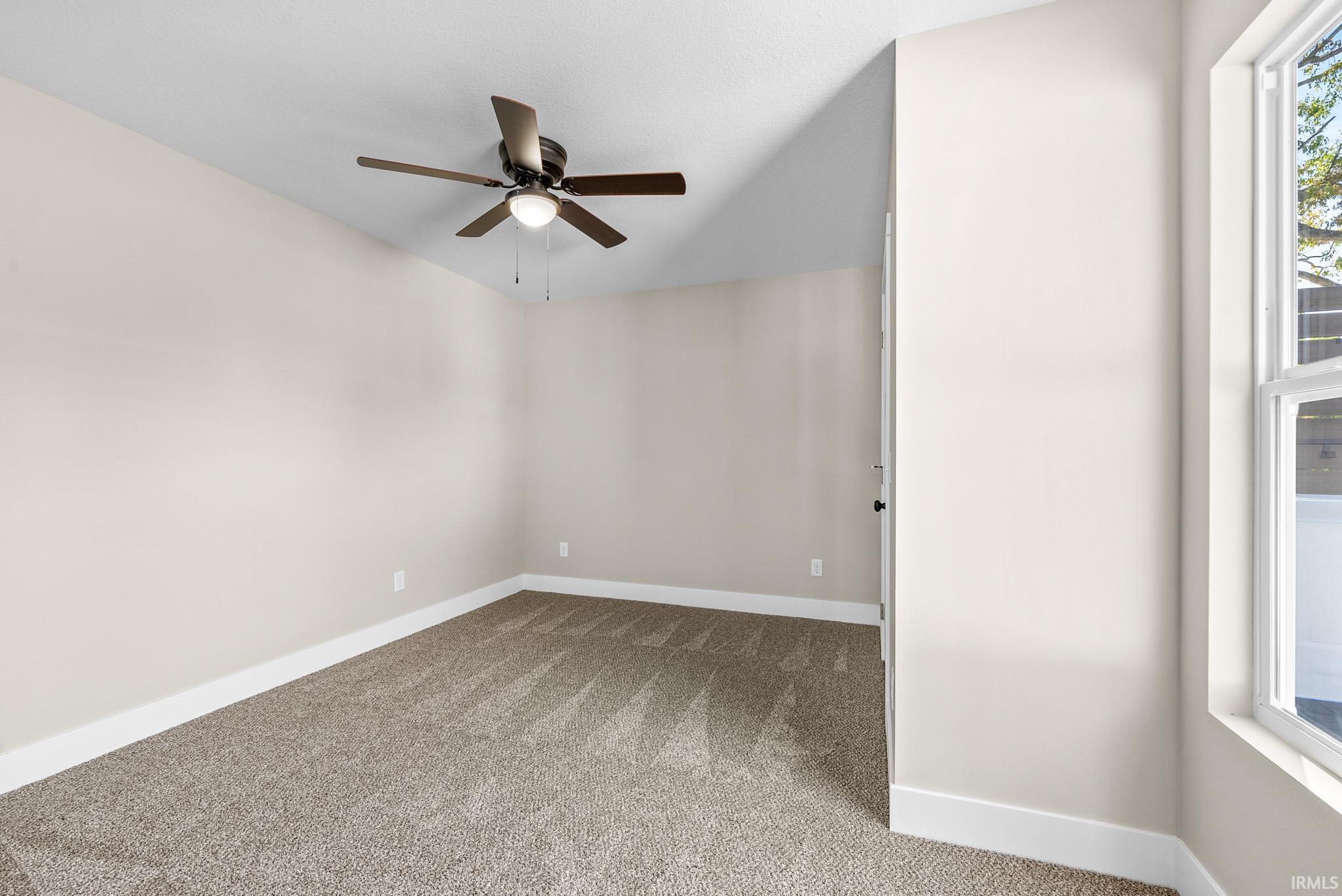 Neutral-toned room featuring a ceiling fan with integrated lighting, a large window, wall-to-wall carpeting, and white baseboards