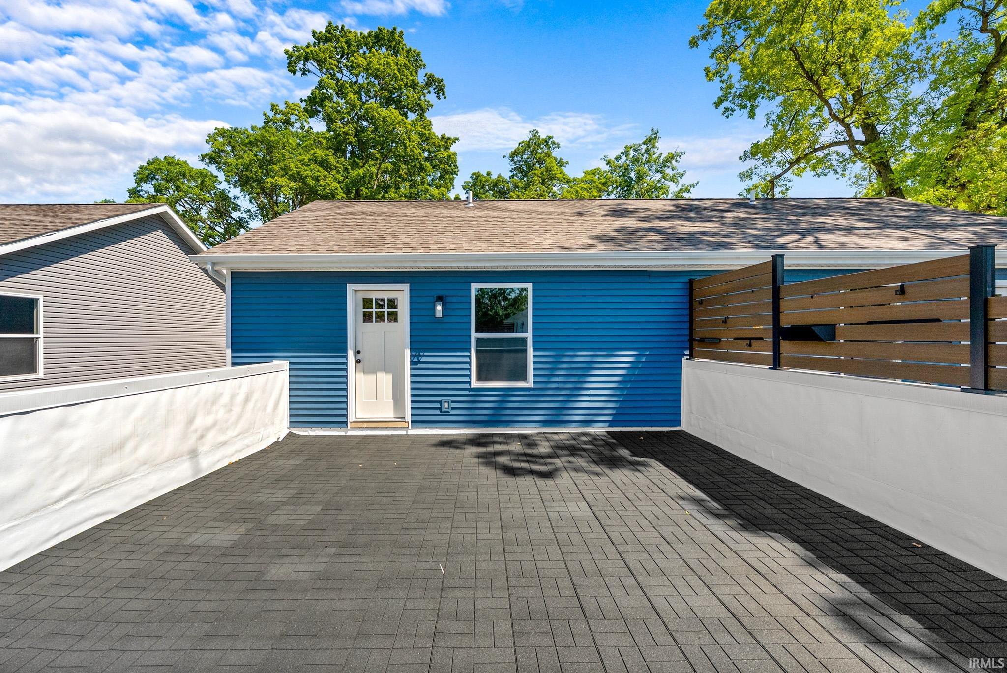 Exterior featuring blue siding, white trim, a white paneled door, and a brown shingle roof