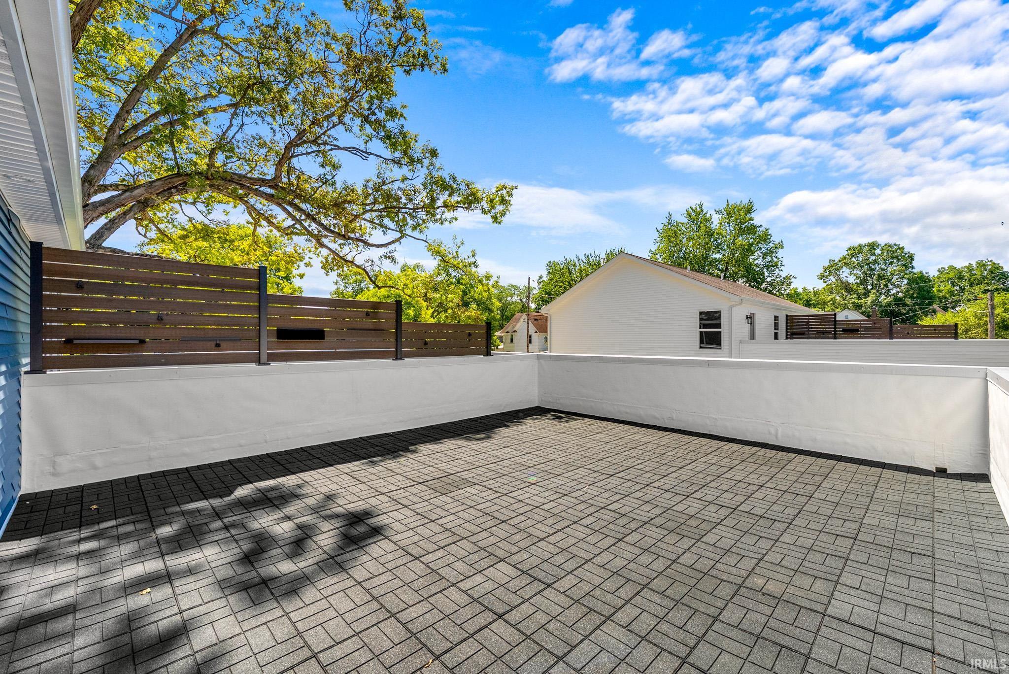 Expansive outdoor patio featuring paver flooring, white stucco walls, and a modern horizontal slat privacy fence