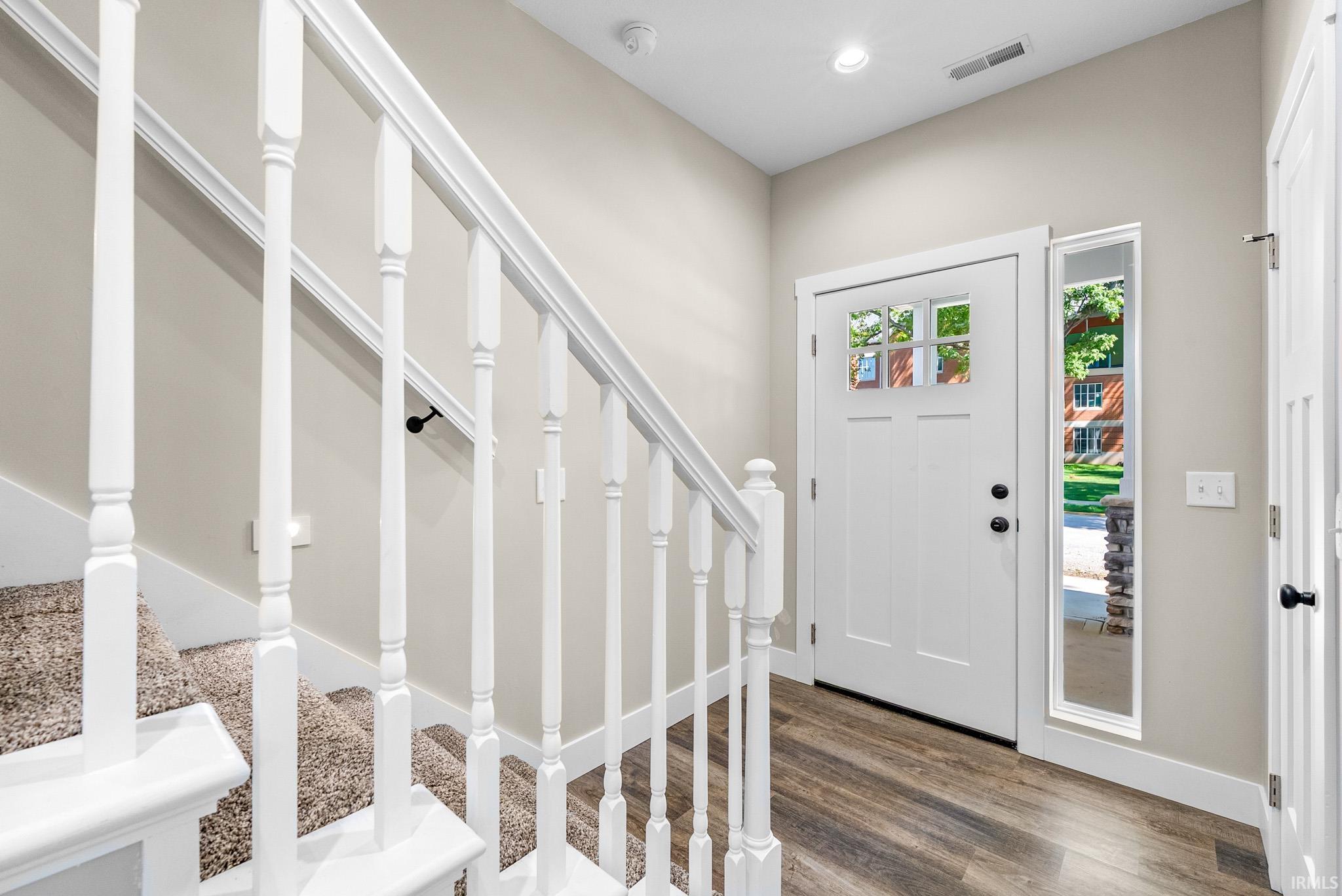 Entryway featuring wood-finish flooring, a white paneled door with glass inserts, a sidelight window, and a carpeted staircase with white balusters