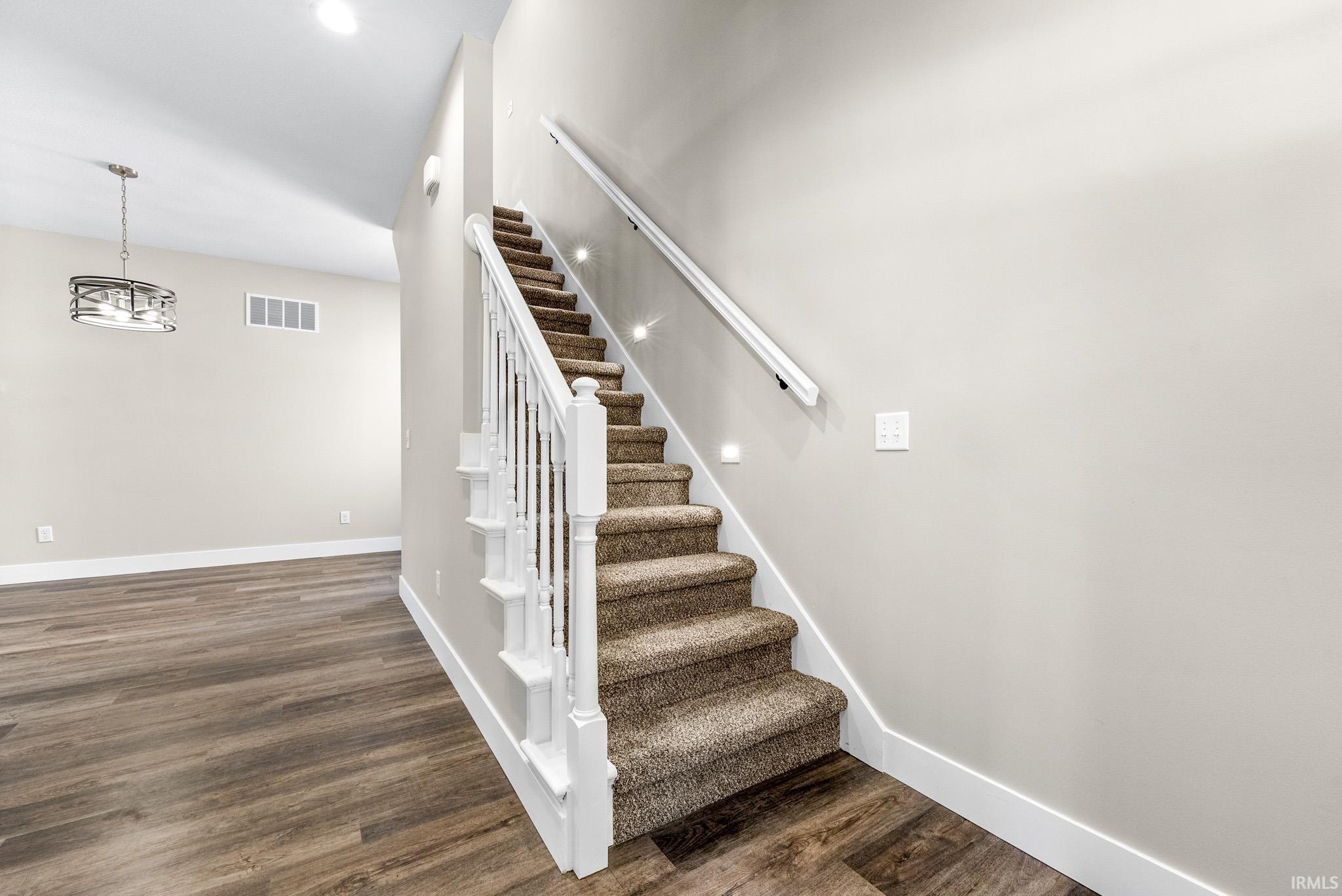 Carpeted staircase with white balusters and handrail, featuring recessed wall lighting and wood-finish flooring