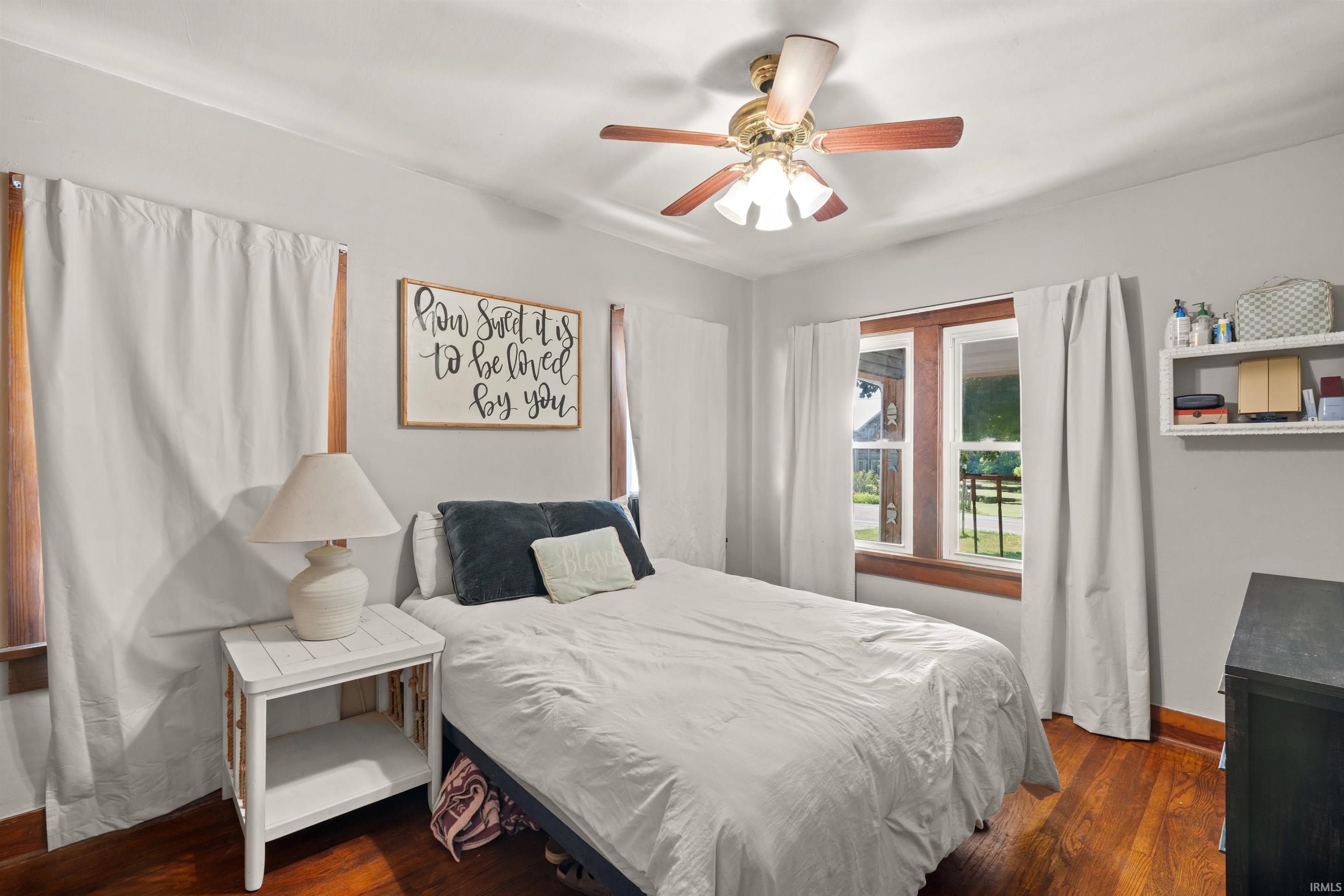 Bedroom featuring wood-finish flooring, a ceiling fan with integrated lighting, and a window with wood trim