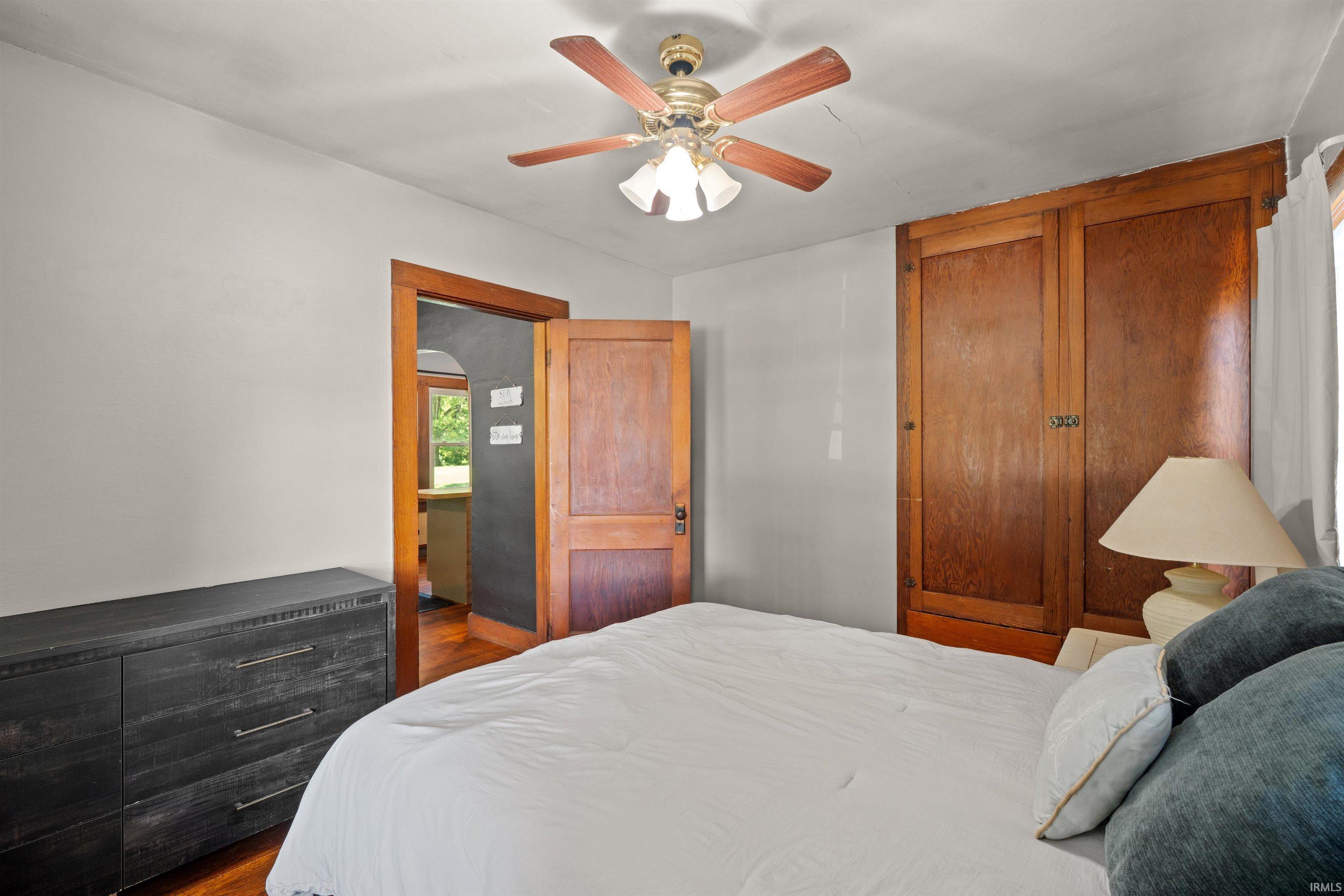Interior room featuring light gray walls, wood-finish flooring, a ceiling fan with integrated lighting, and a built-in wood wardrobe