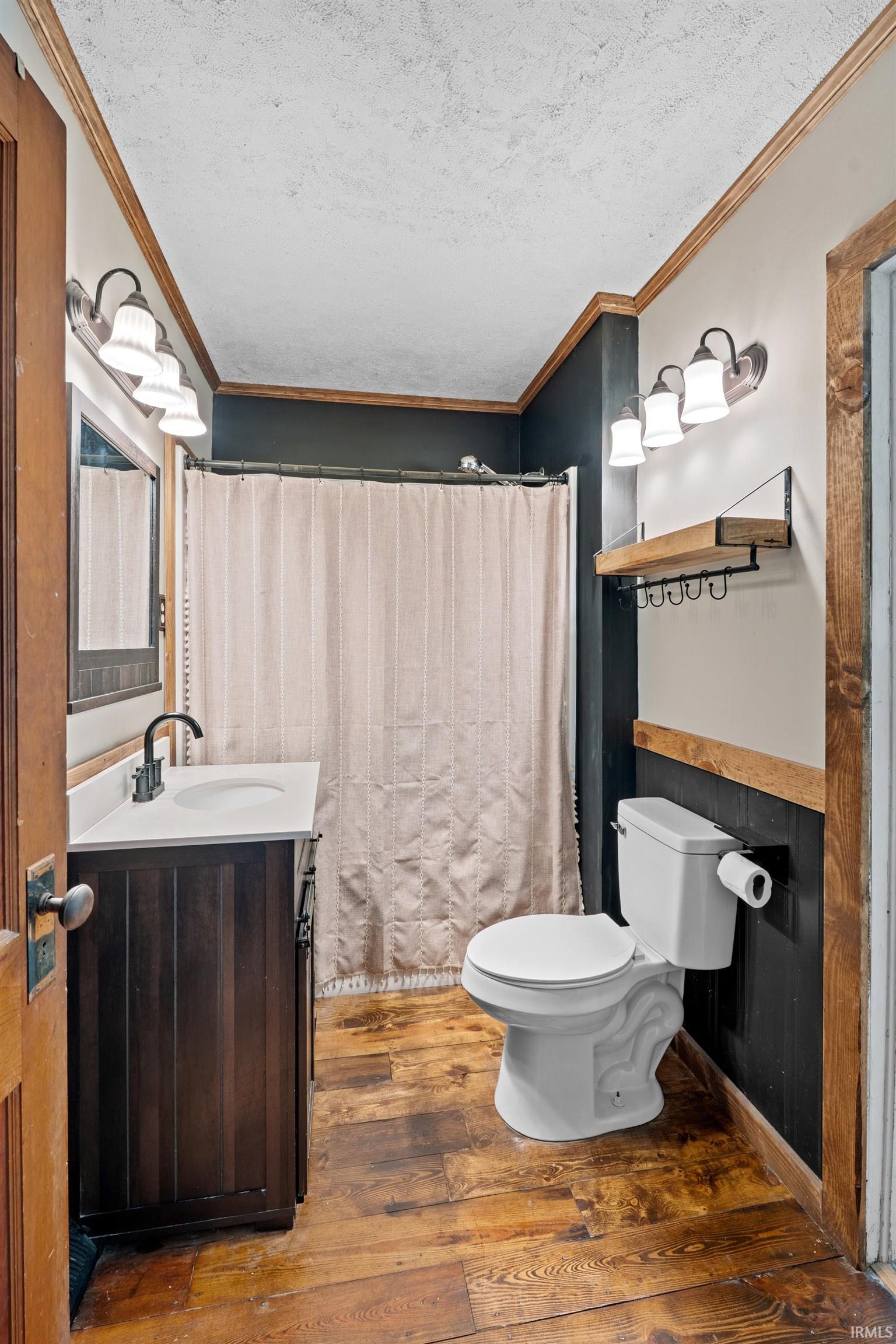 Bathroom featuring wood-finish flooring, a dark wood-tone vanity with a white countertop and rectangular sink, and two three-light vanity fixtures