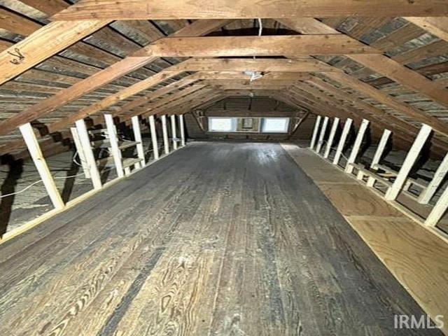 Spacious attic area featuring exposed wooden rafters and plank flooring
