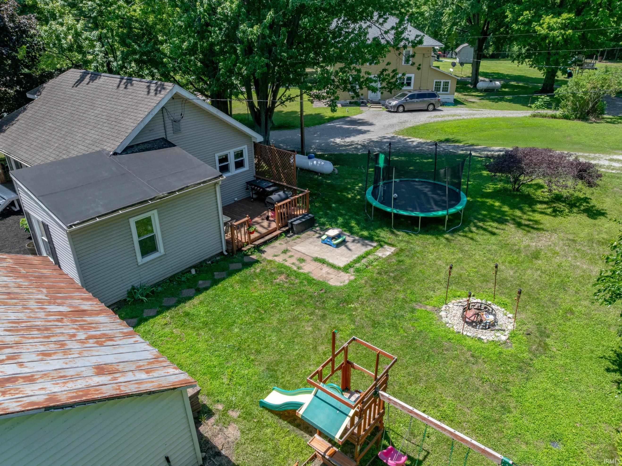 Expansive green lawn with a fire pit area, a wooden playset with a slide, and a multi-level deck