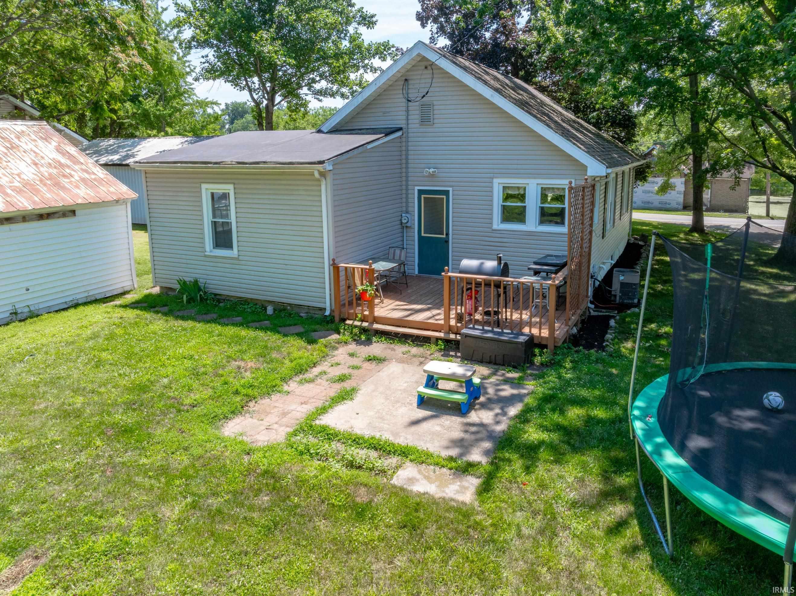 Rear exterior featuring a wood deck, concrete patio, and a grass lawn