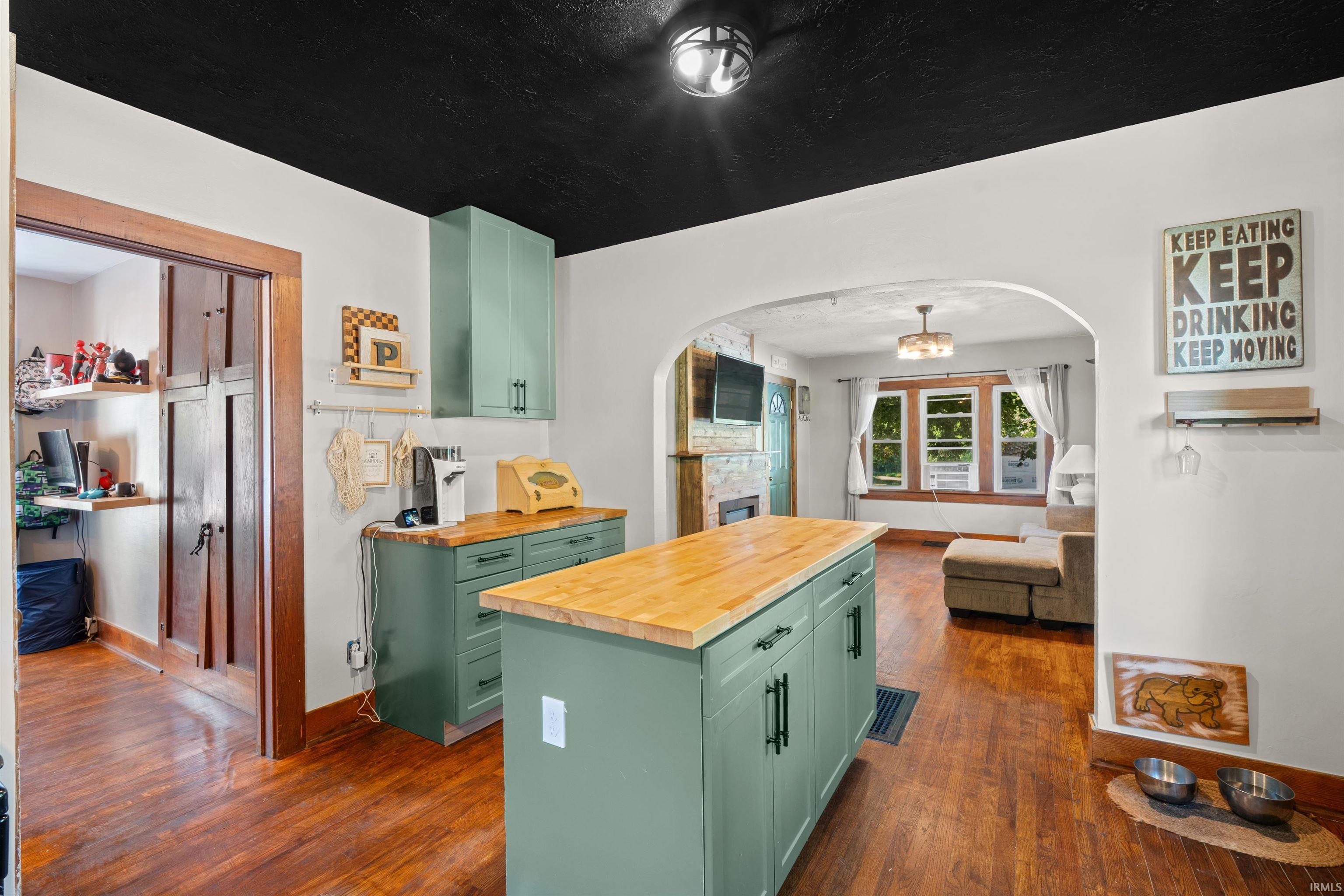 Kitchen featuring a central island with wood-finish countertop, green cabinetry, hardwood flooring, and a black painted ceiling