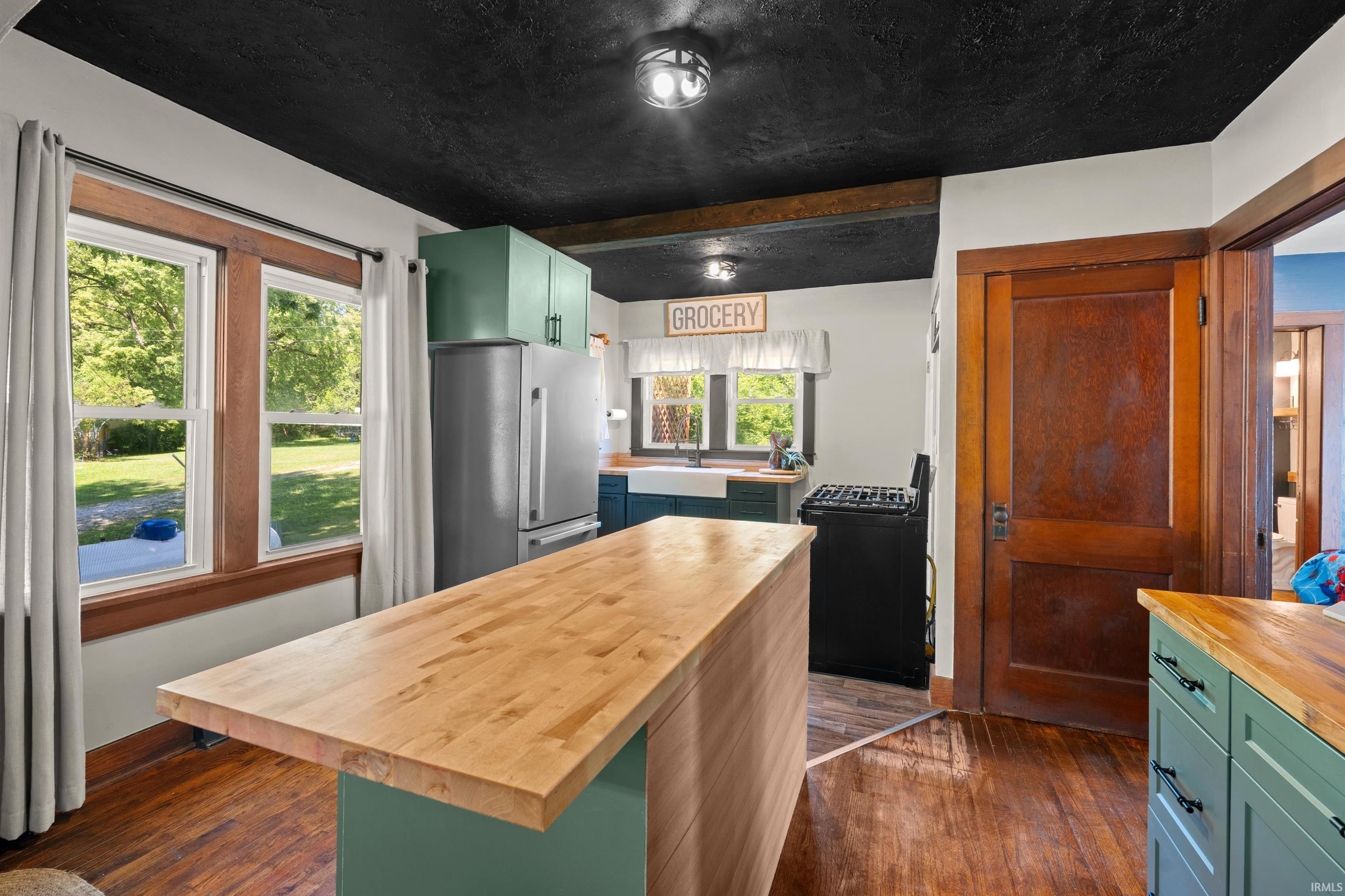 Kitchen featuring a wood-finish floor, a large center island with a wood countertop, stainless steel refrigerator, and a dark ceiling