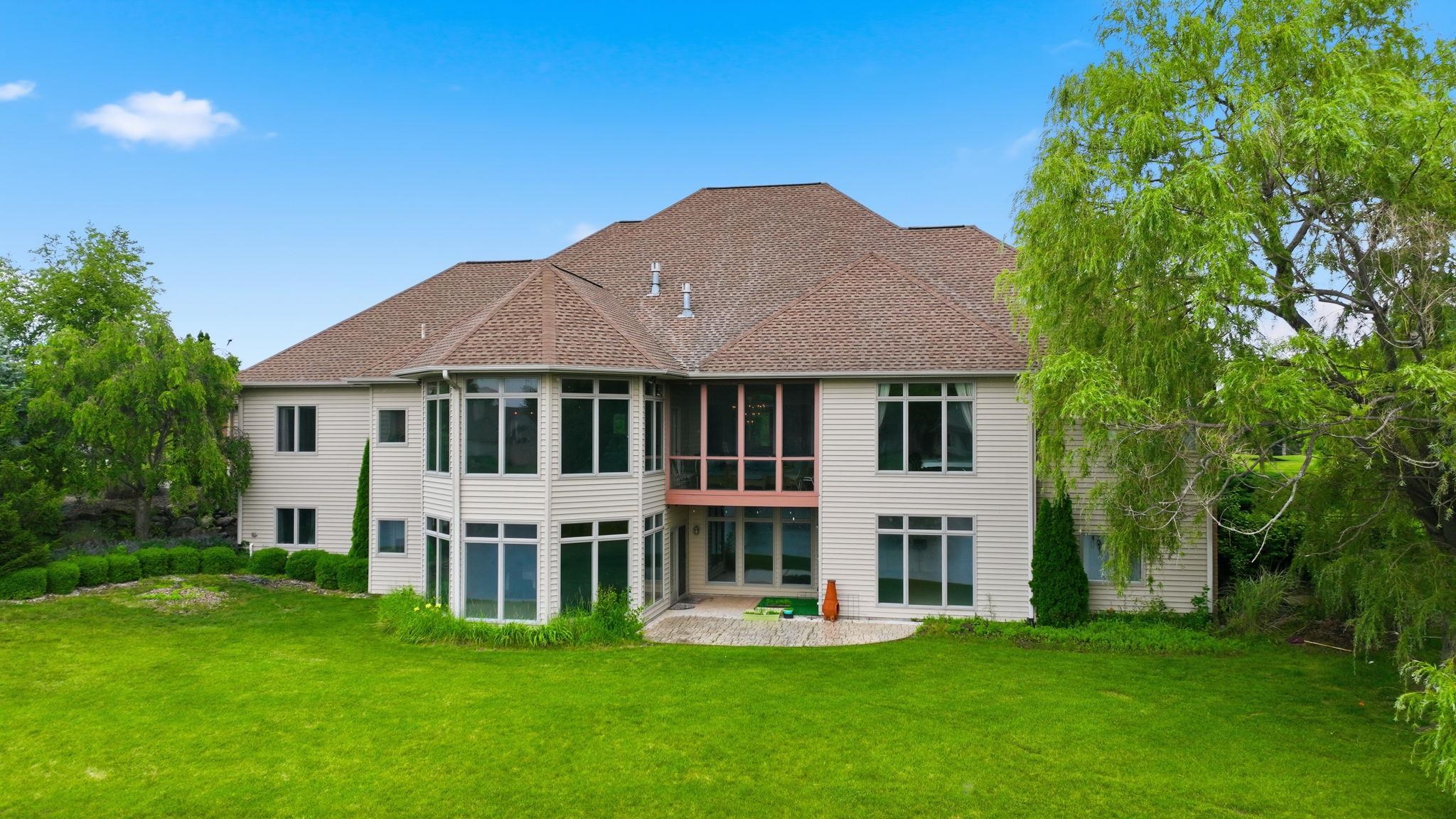 Expansive rear elevation featuring multiple large windows, a screened-in porch, and a stone patio