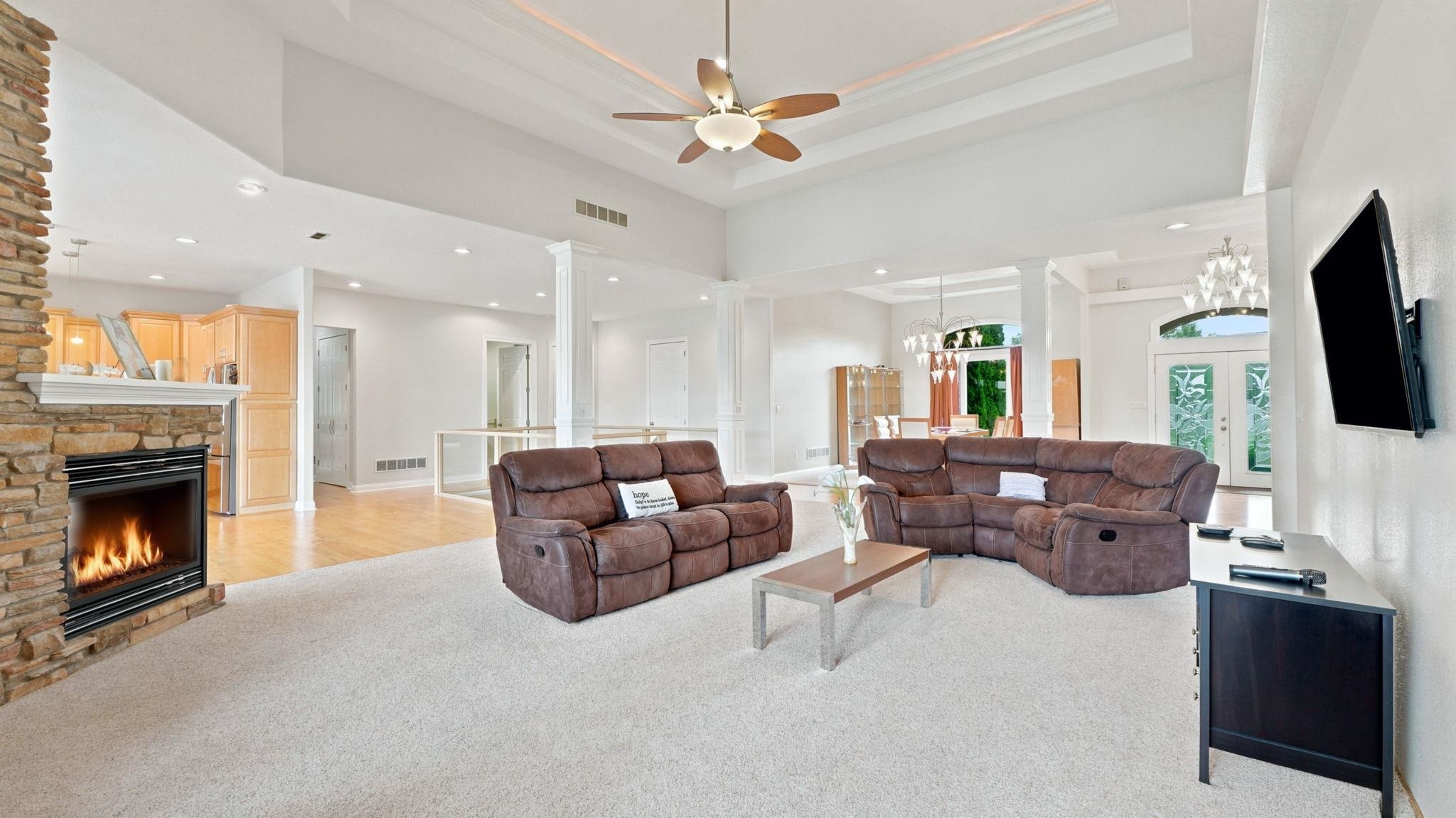 Spacious living area featuring a stacked stone fireplace with a white mantel, vaulted ceilings, and a ceiling fan
