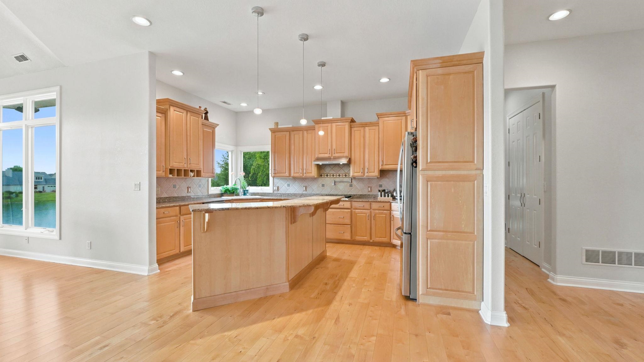 Expansive kitchen featuring light wood cabinetry, a central island with an extended countertop, and stainless steel appliances