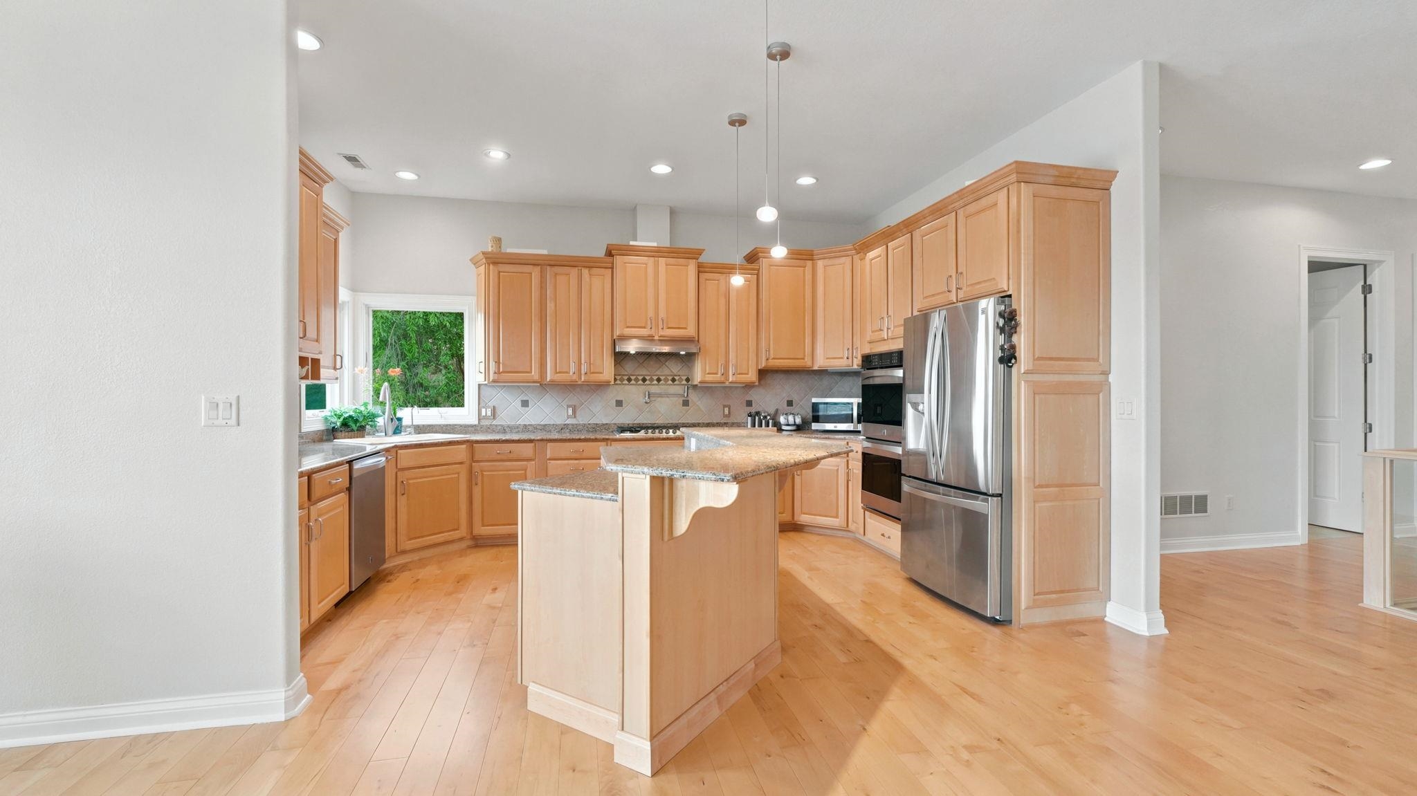 Kitchen featuring light wood cabinetry, stainless steel appliances, a center island with pendant lighting, wood-finish flooring, and a window above the sink
