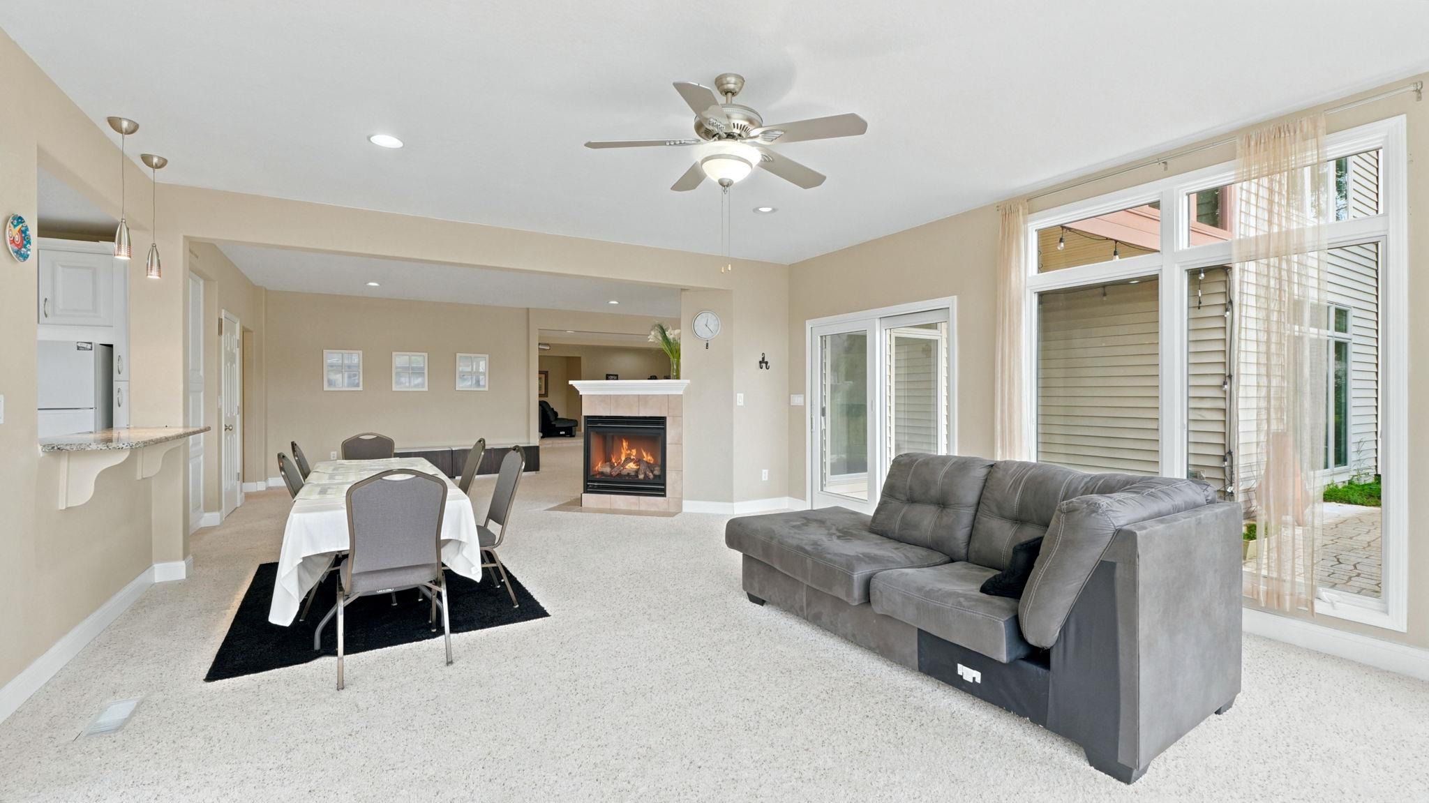 Spacious room featuring light carpeting, a built-in gas fireplace with a tiled surround, recessed lighting, and a ceiling fan