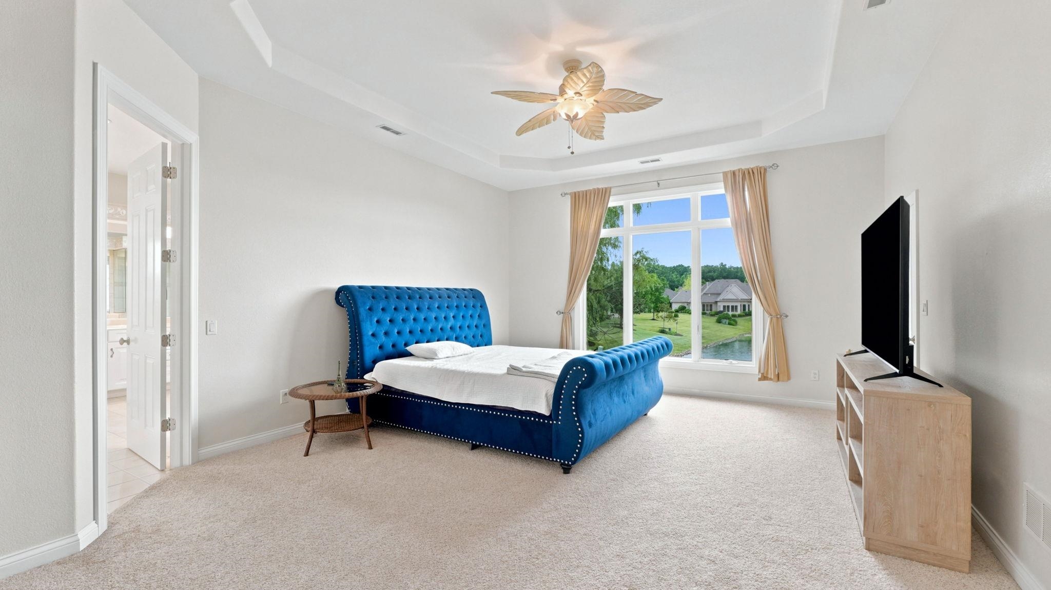 Spacious room featuring a tray ceiling, ceiling fan, and large window offering exterior views