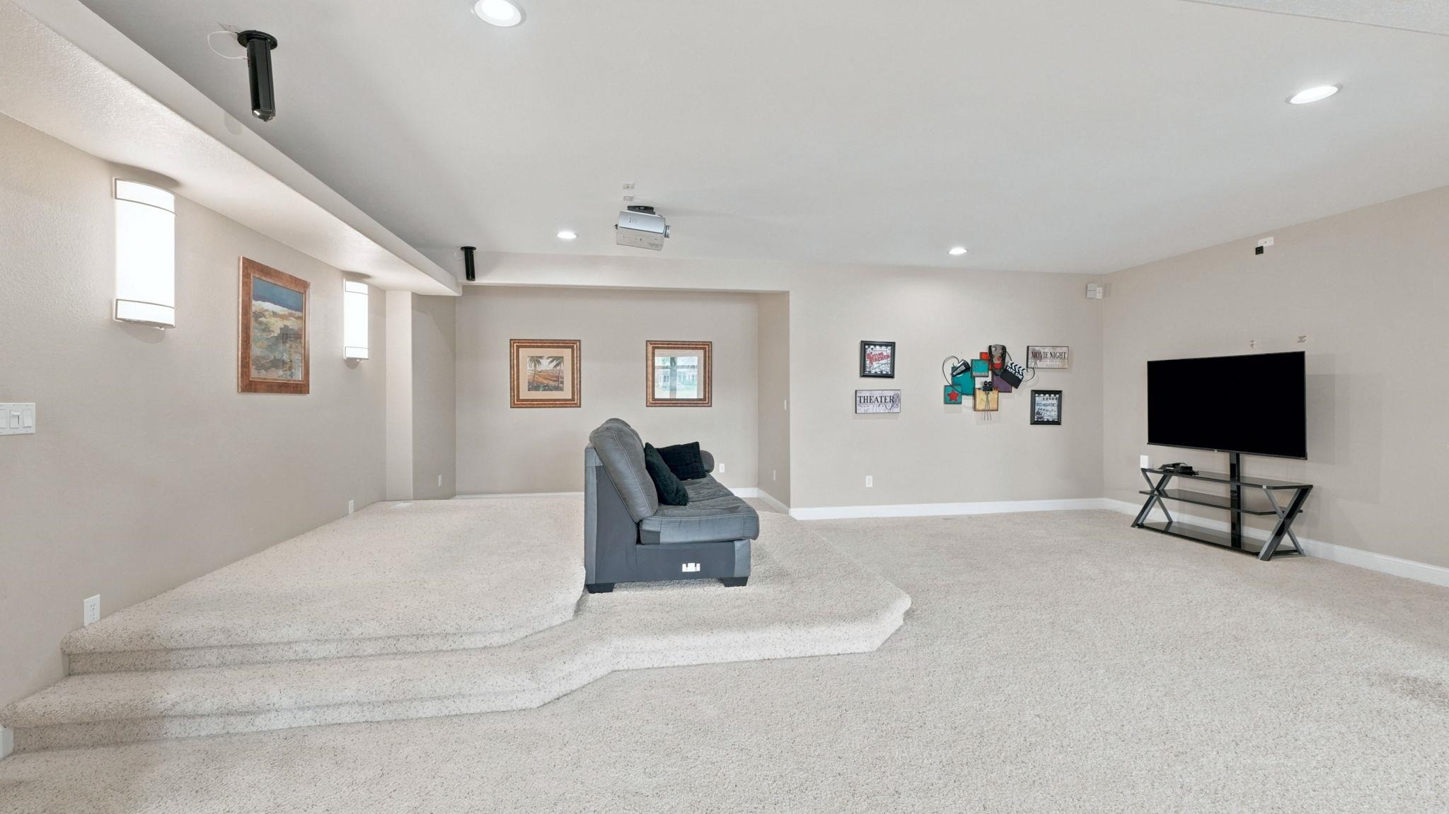 Multi-level media room featuring recessed lighting, a tiered carpeted floor, and a mounted projector