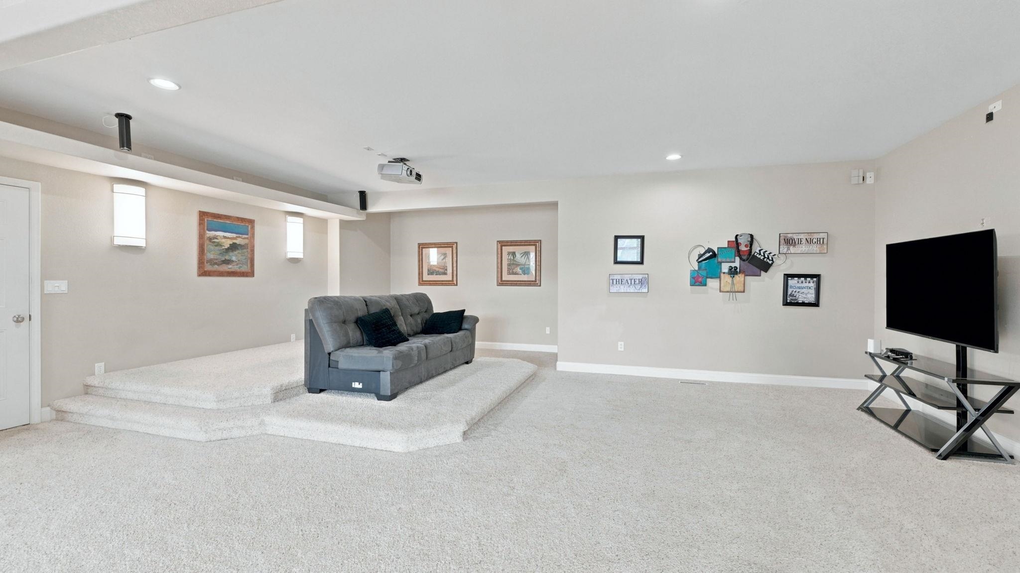 Carpeted recreation room featuring a tiered seating area with a built-in projector, recessed lighting, and wall-mounted sconces