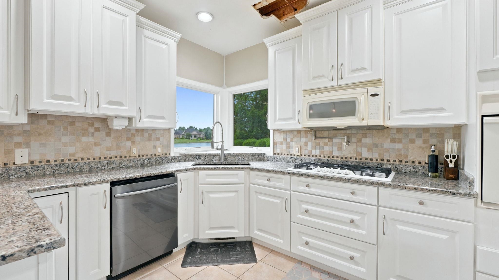 Kitchen featuring white cabinetry, granite-finish countertops, stainless steel dishwasher, gas cooktop, and a corner window with exterior water views