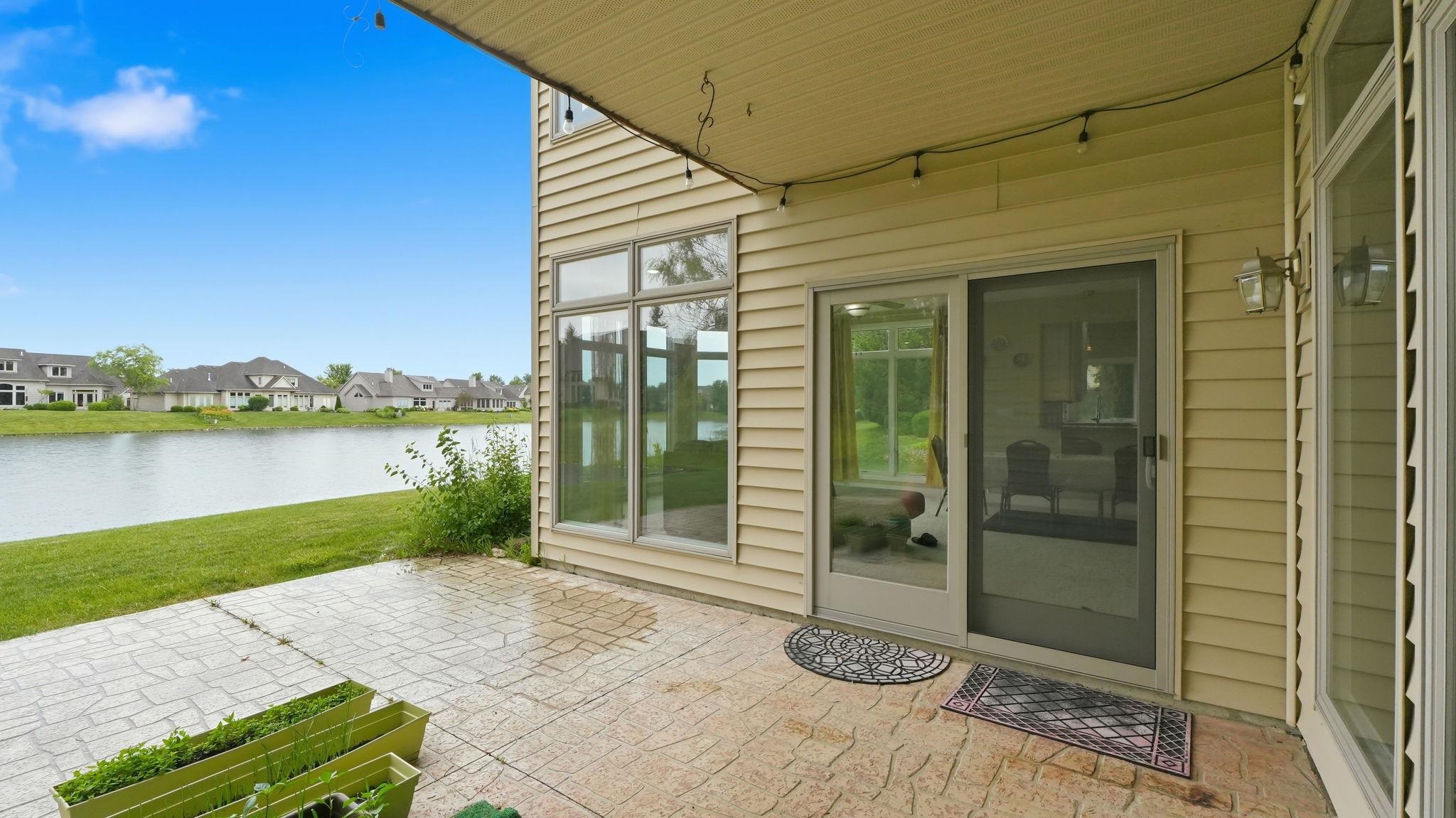 Stamped concrete patio featuring waterfront access, expansive green space, and a sliding glass door entry point