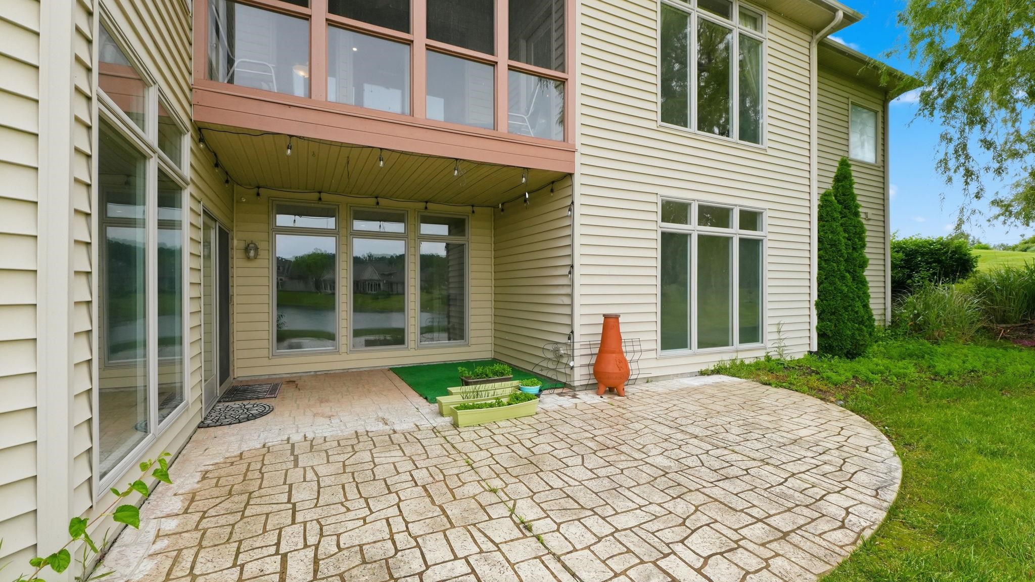 Exterior featuring light-colored horizontal siding, a stone-patterned patio, and multiple large windows