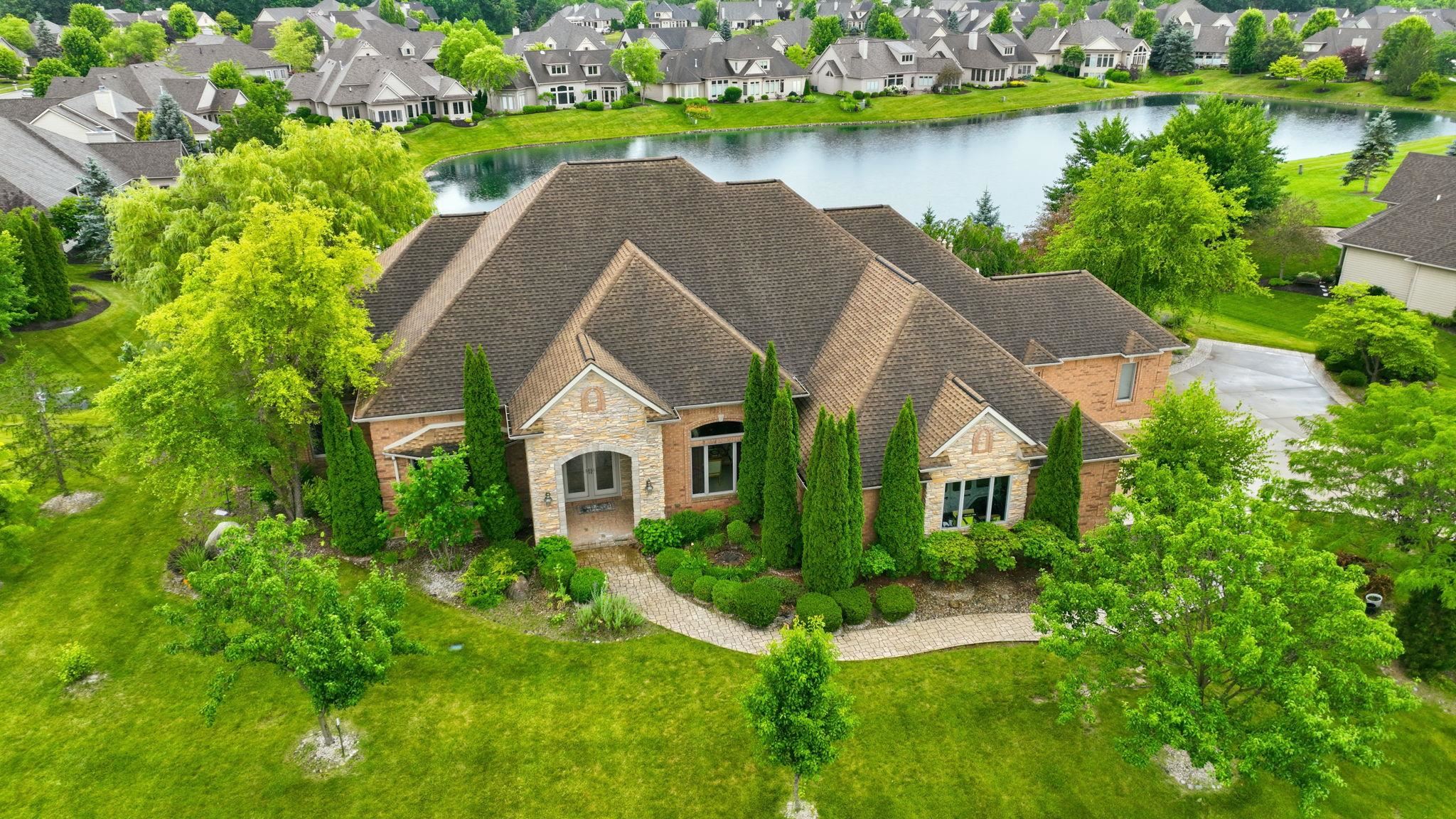 Brick and stone exterior residence featuring a multi-gabled roof, mature landscaping, a curved paver walkway, and a prominent front entry